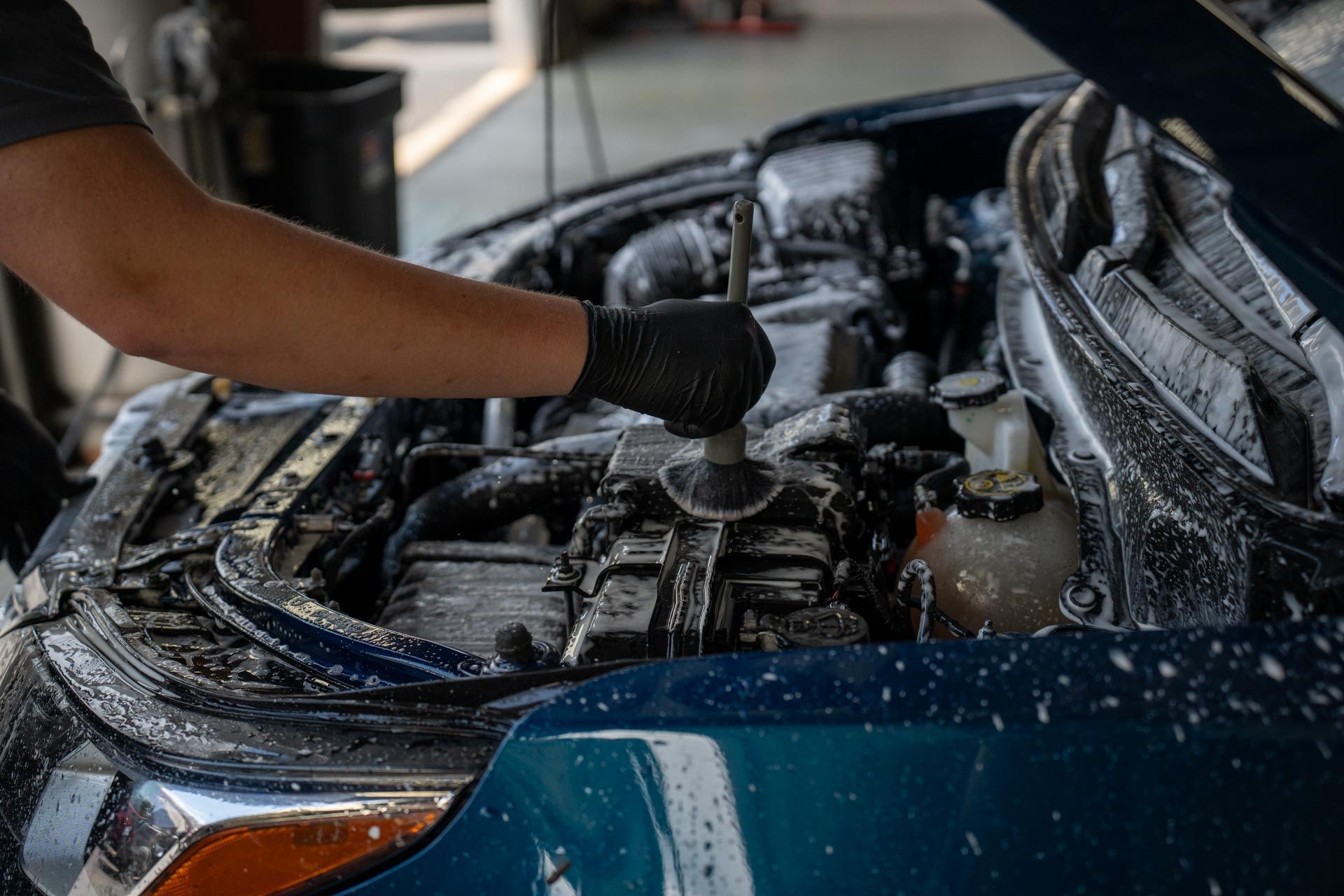 A man is cleaning the engine of a car with a brush.