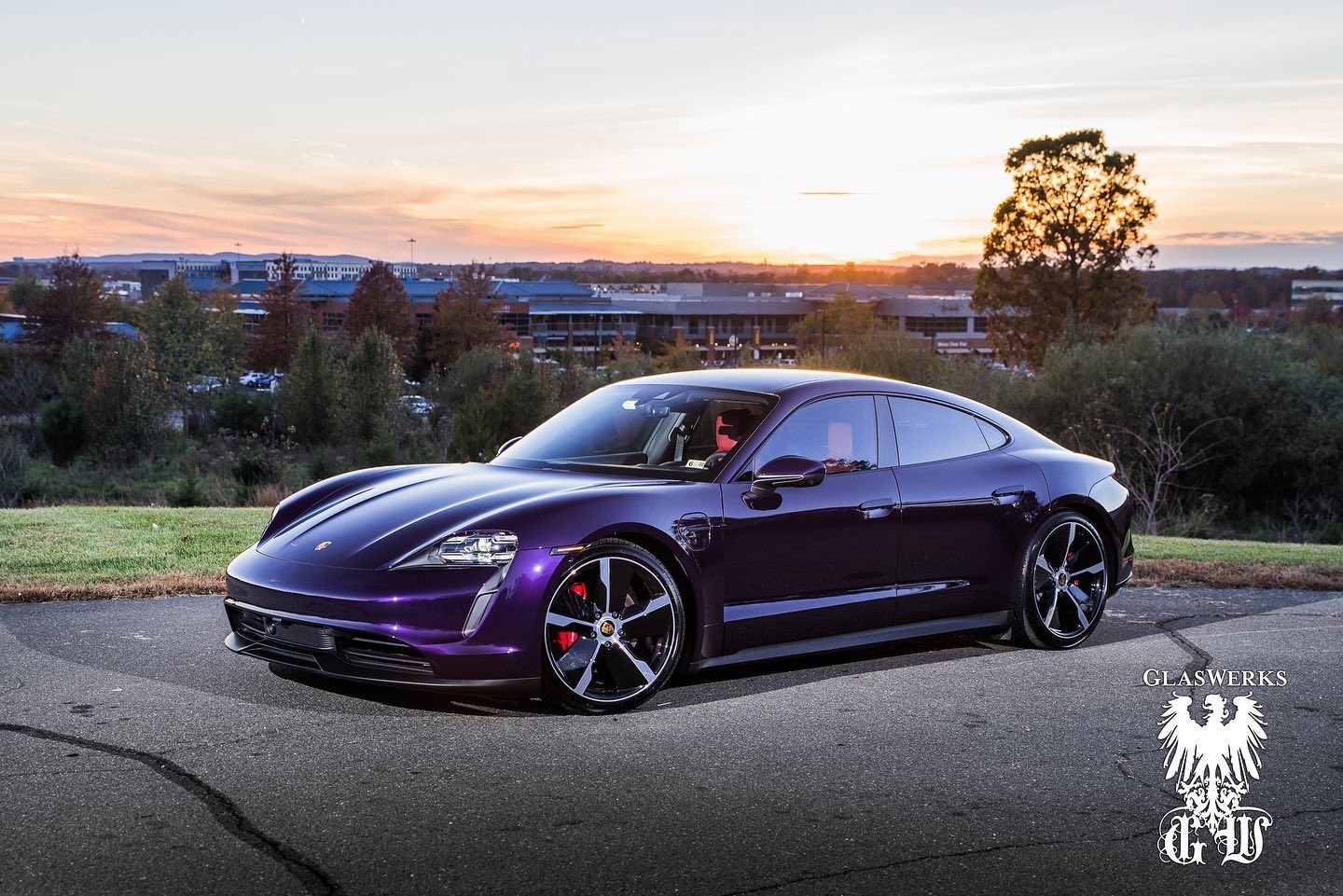 A purple porsche taycan is parked on the side of the road at sunset.