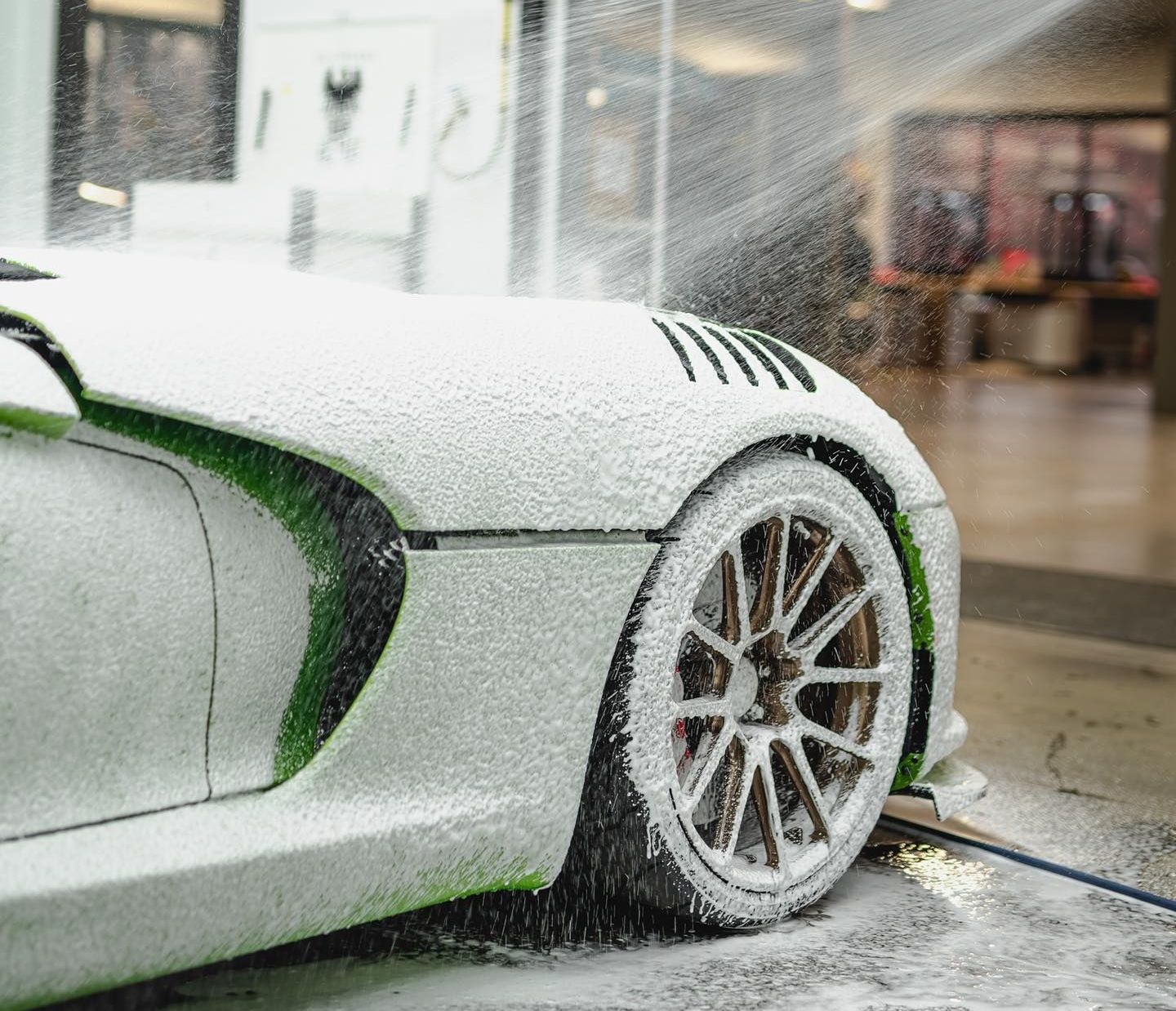 A person is washing a black car with foam.