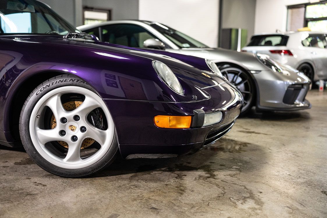 A purple porsche is parked next to a silver porsche in a garage.