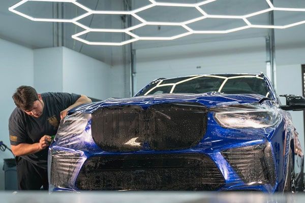 A man is wrapping a blue car in plastic in a garage.