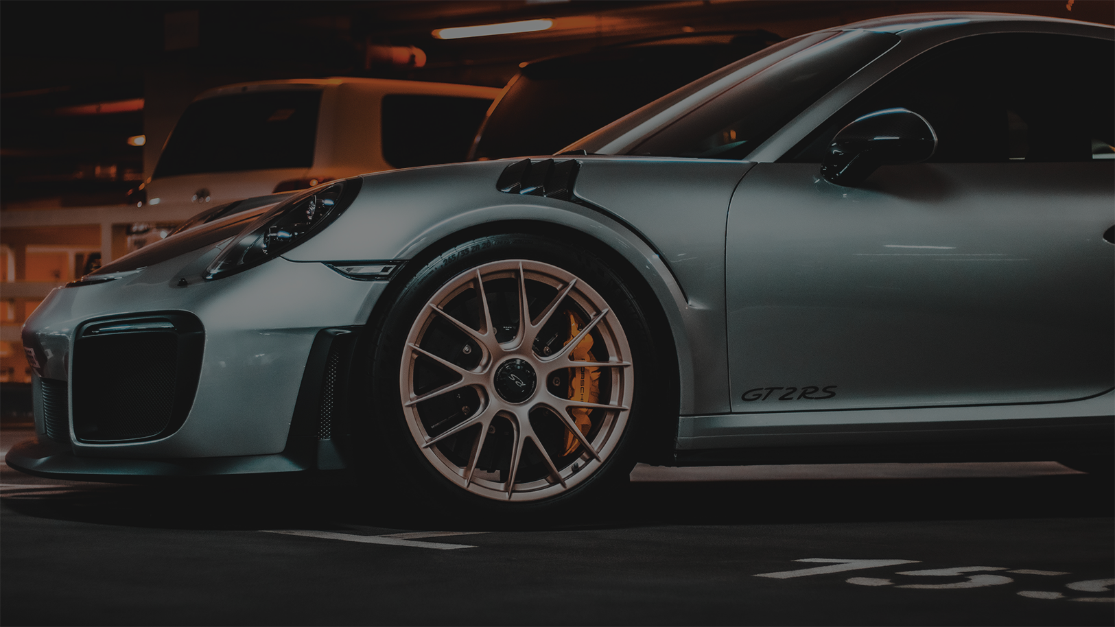 A silver sports car is parked in a parking lot at night.