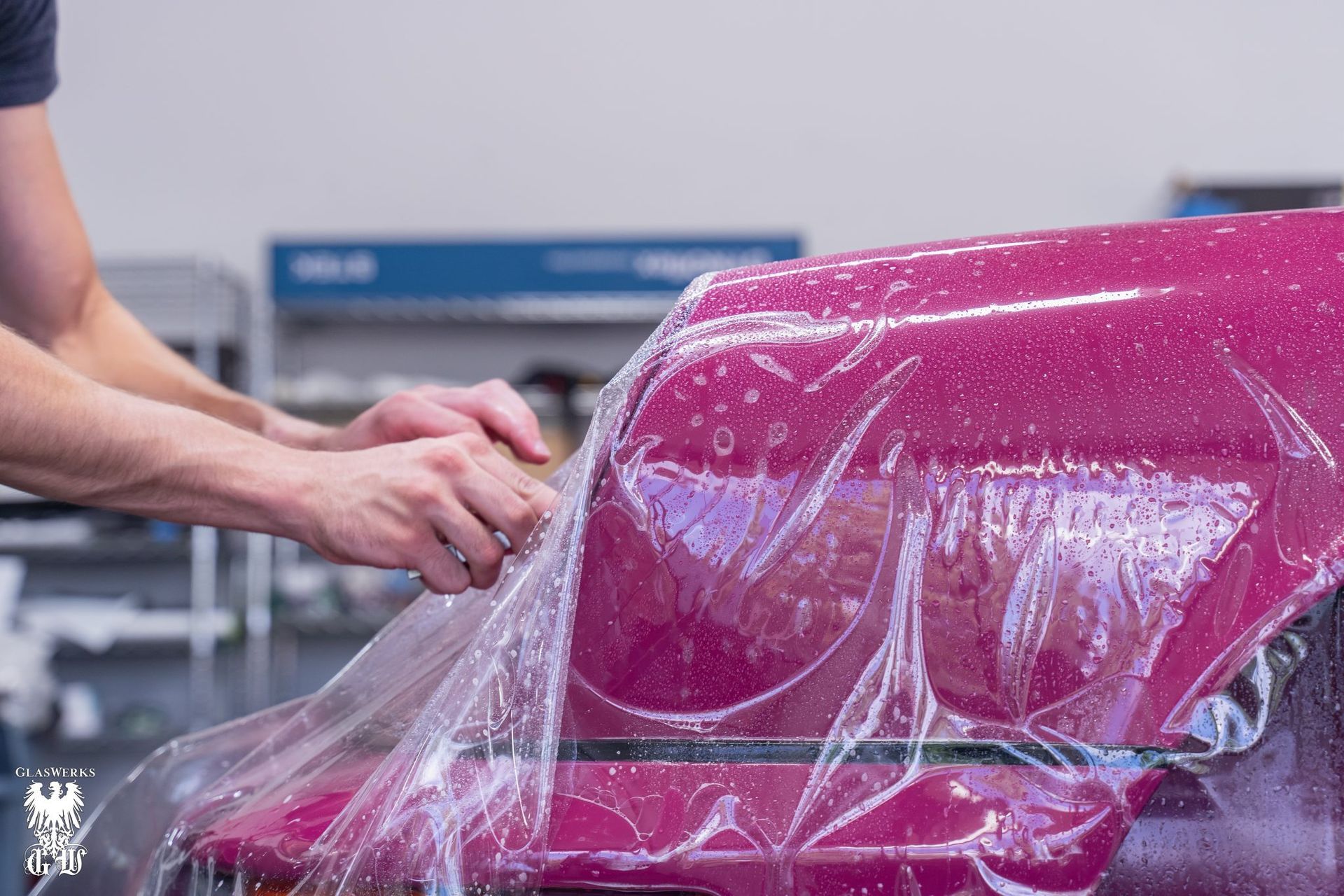 A man is wrapping a pink car with plastic wrap.