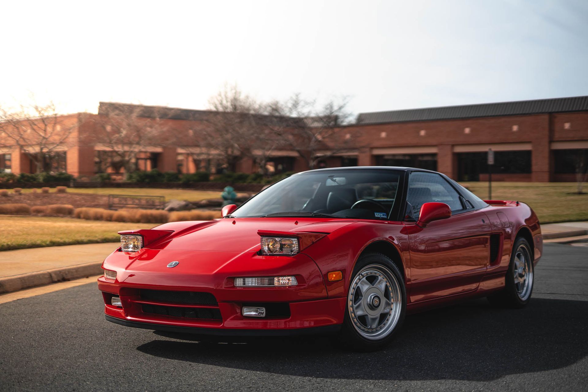 A red sports car is parked on the side of the road in front of a building.