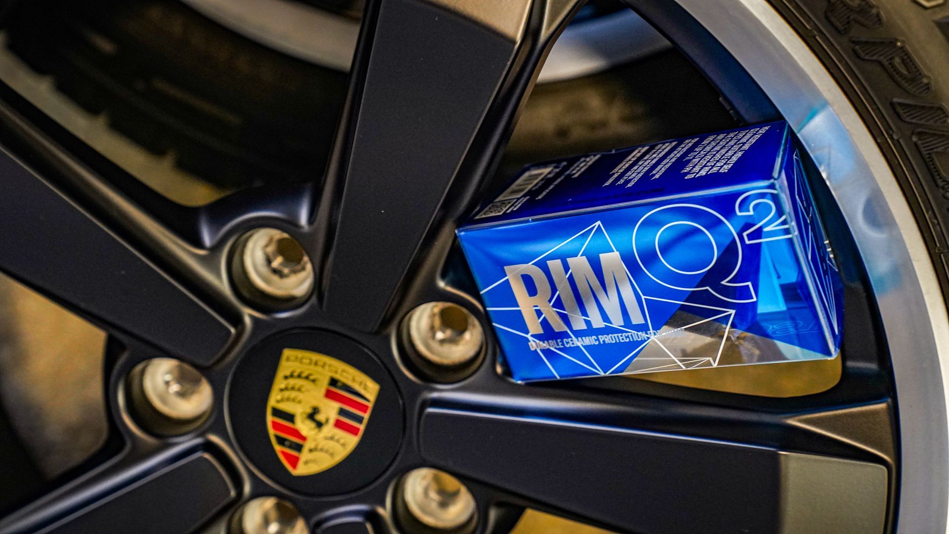 A close up of a porsche wheel with a box of rim cleaner on it.