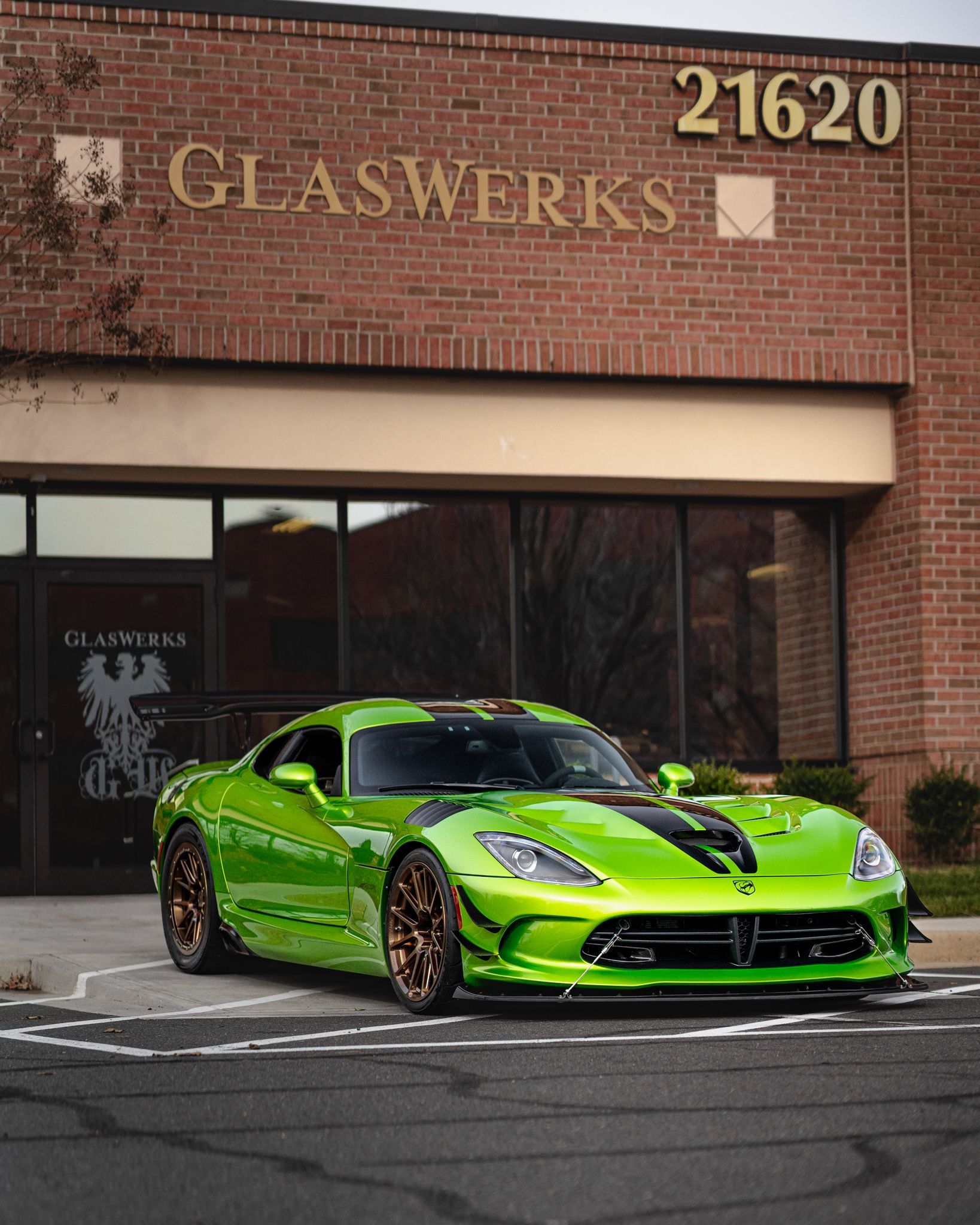 A green sports car is parked in front of a glassworks building