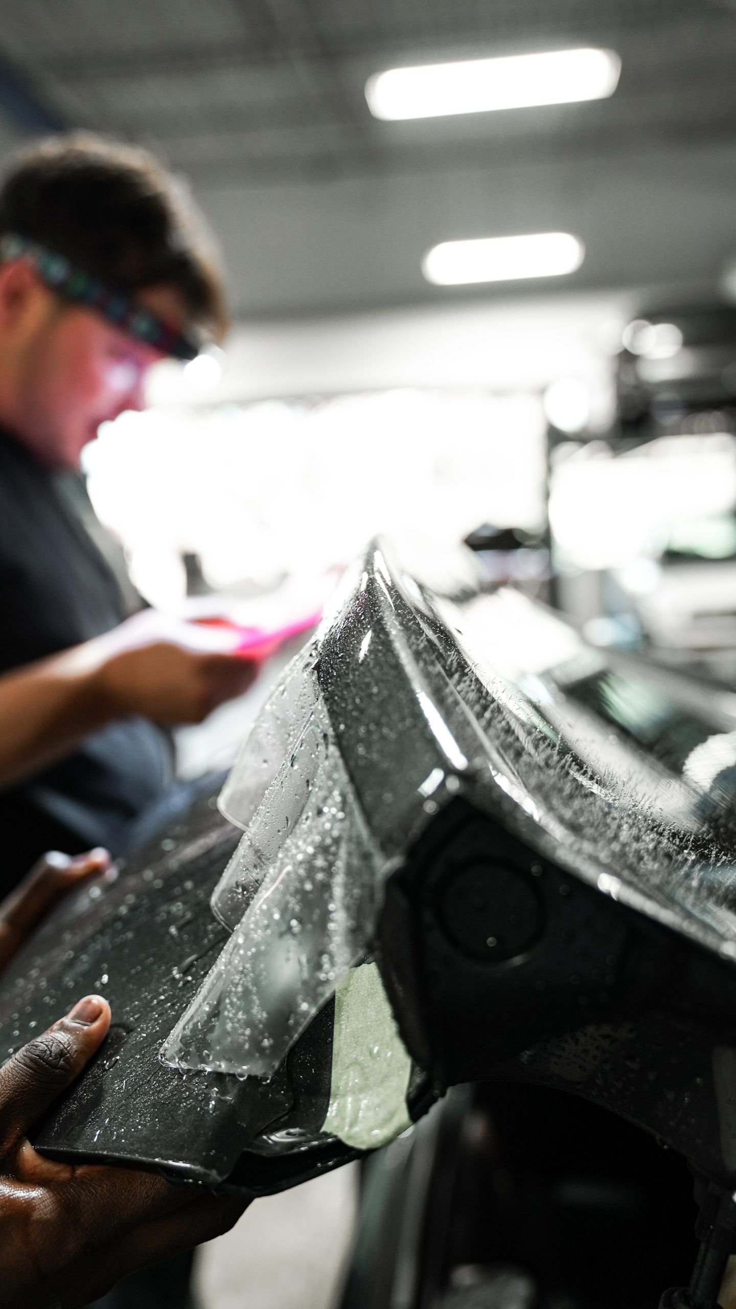 A man is applying a protective film to the side of a car.