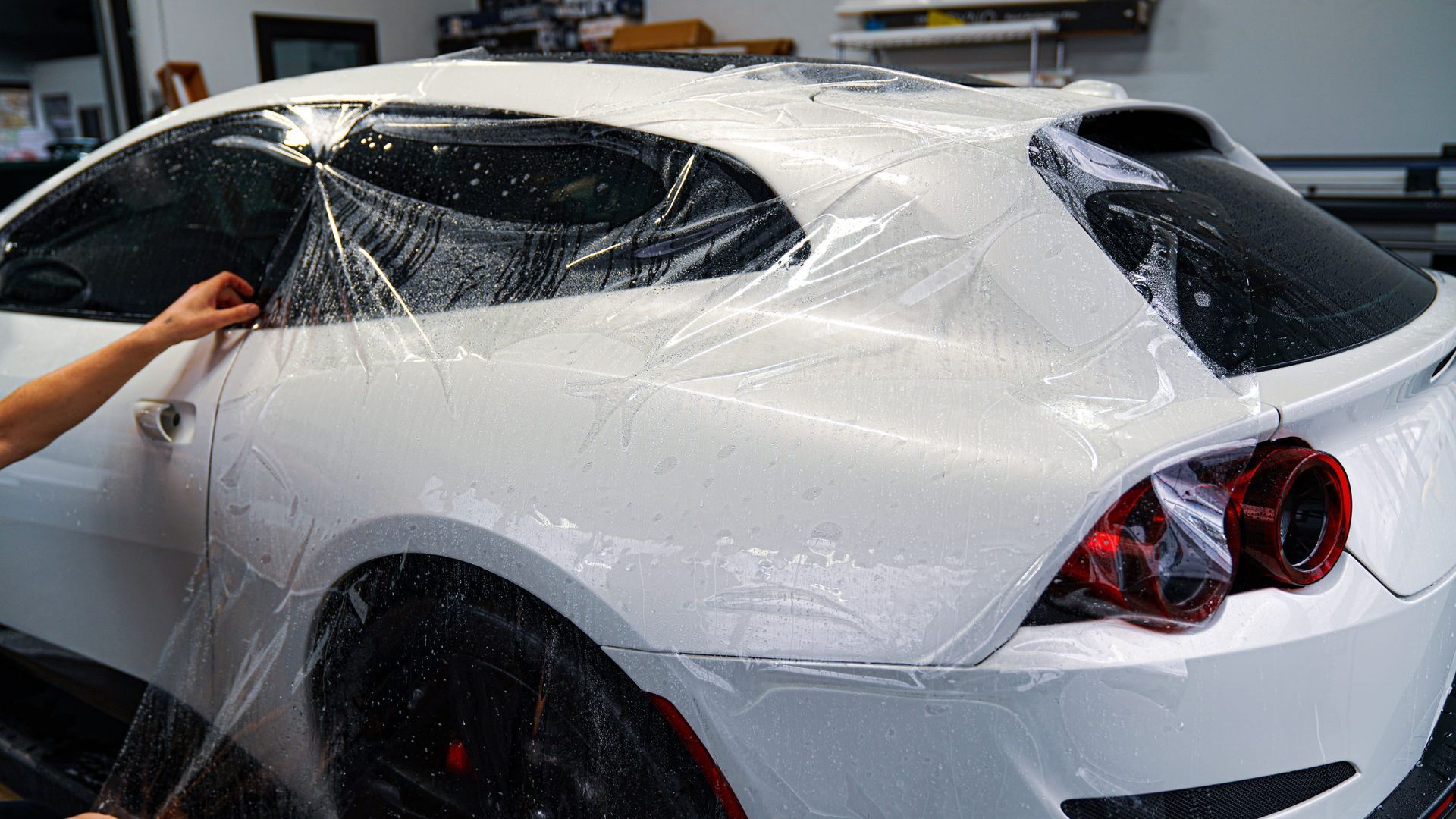 A person is wrapping a white car with plastic wrap.
