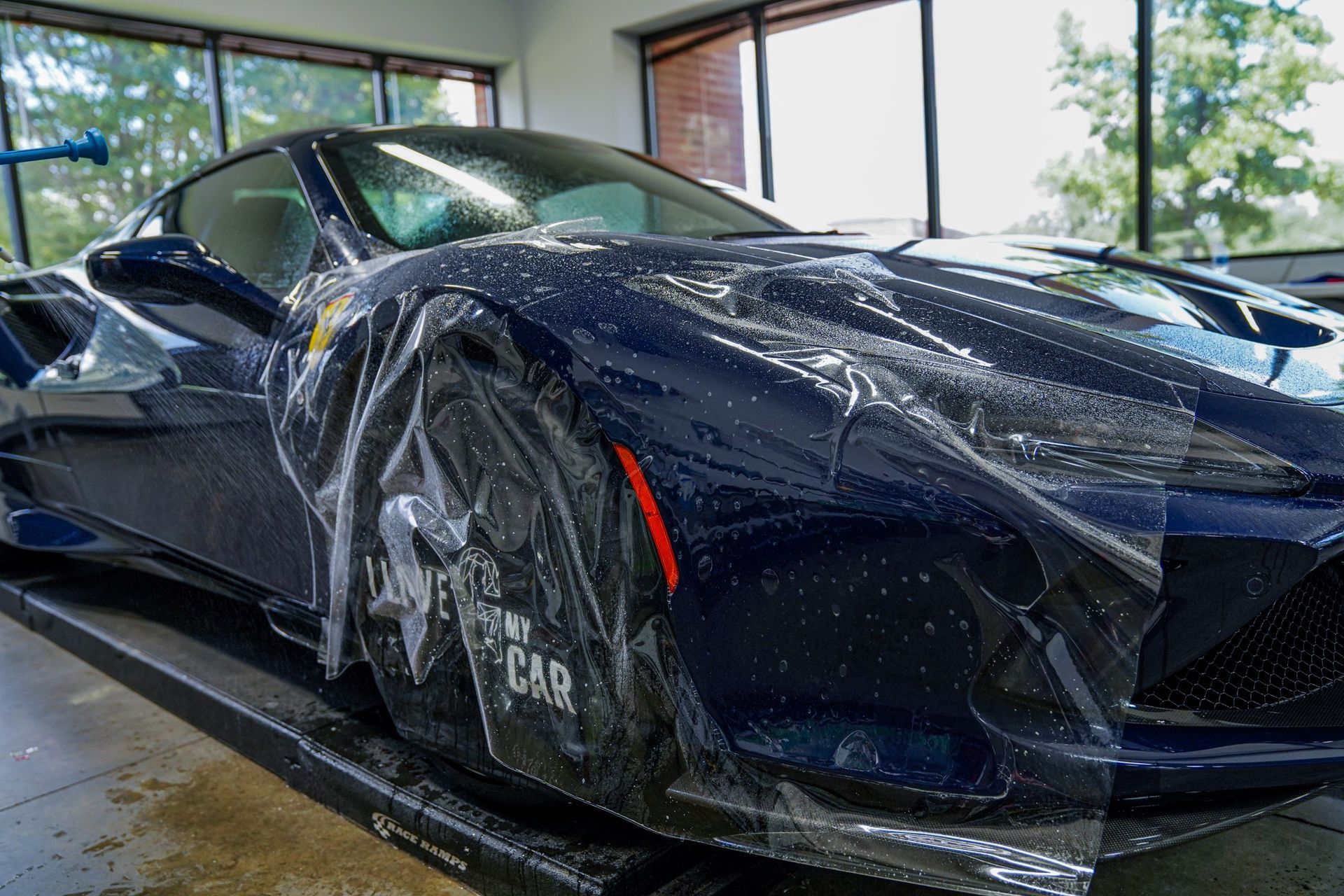 A blue sports car is wrapped in plastic and sitting on a lift.