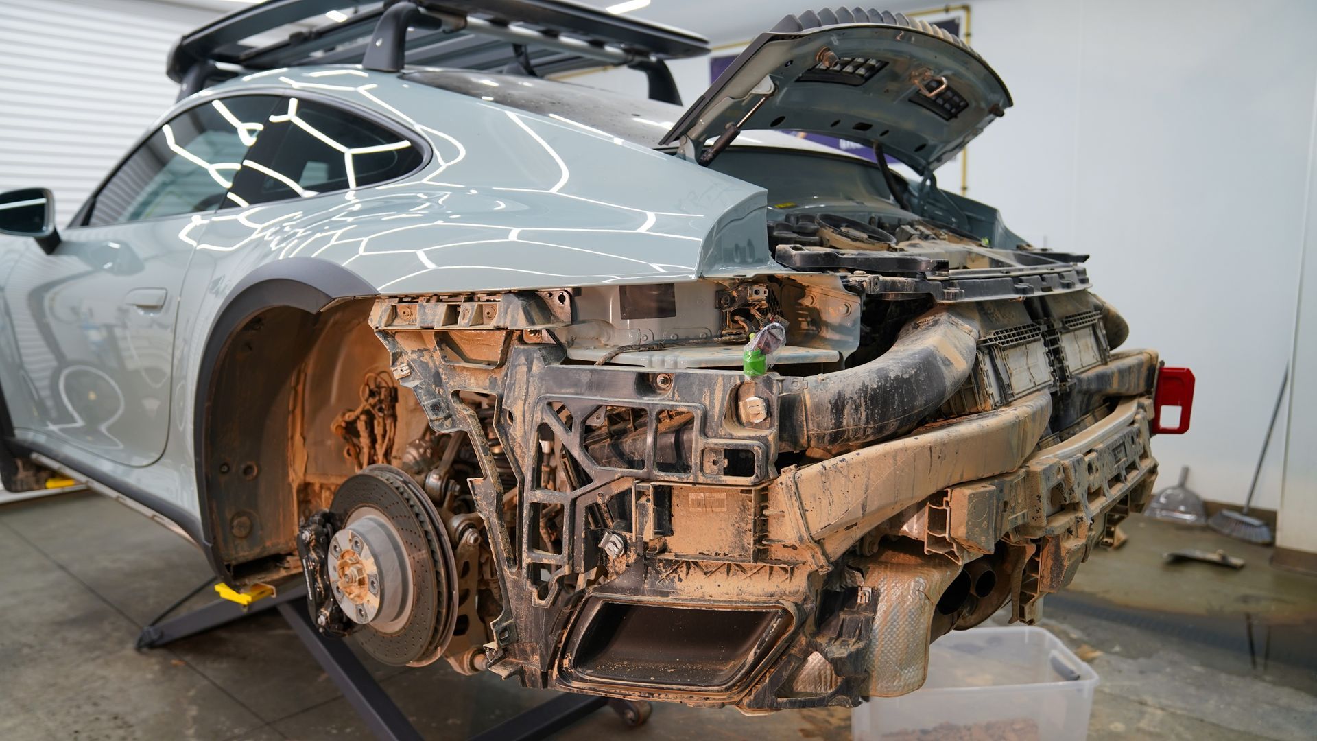 A dirty car is sitting on a lift with the hood open.