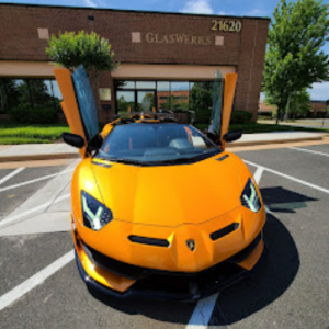 A yellow sports car is parked in front of a glassworks building