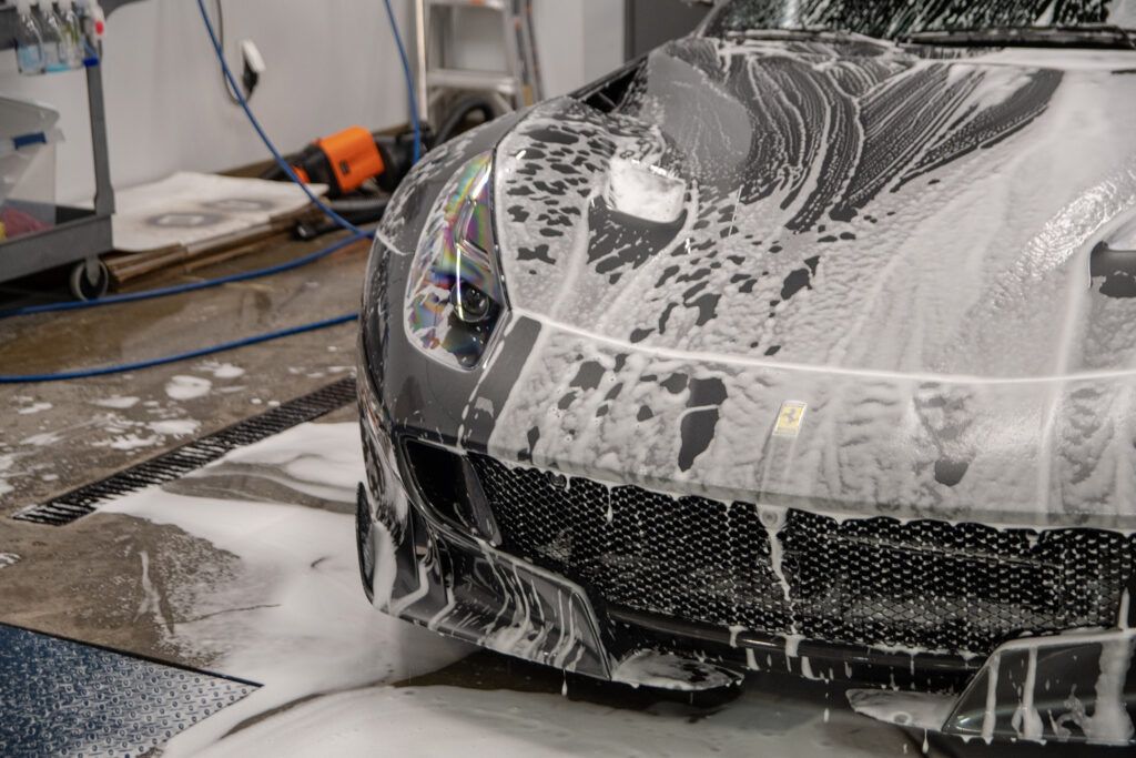 A black sports car is covered in foam in a garage.