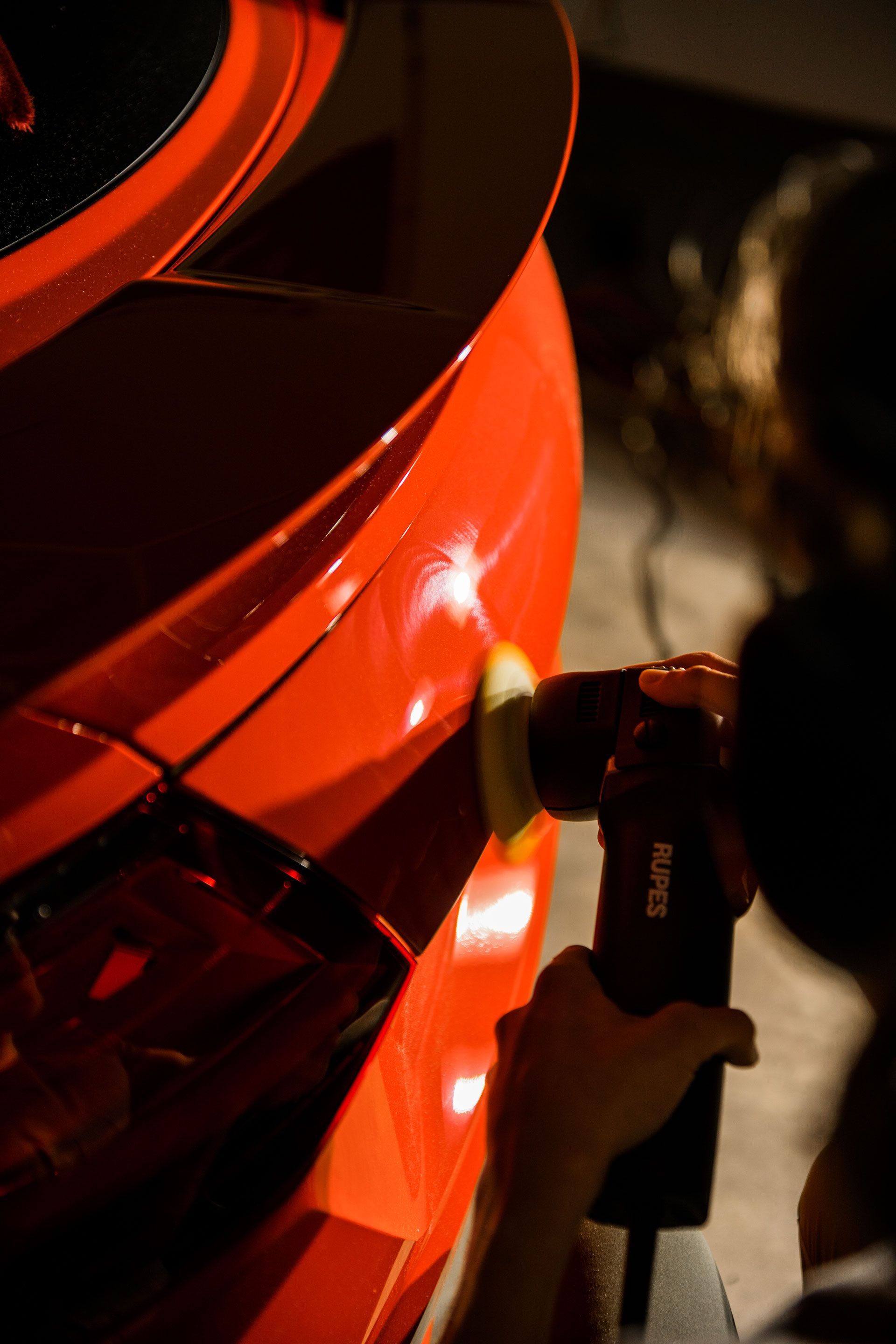 A person is polishing a red car with a polisher that says ksr on it