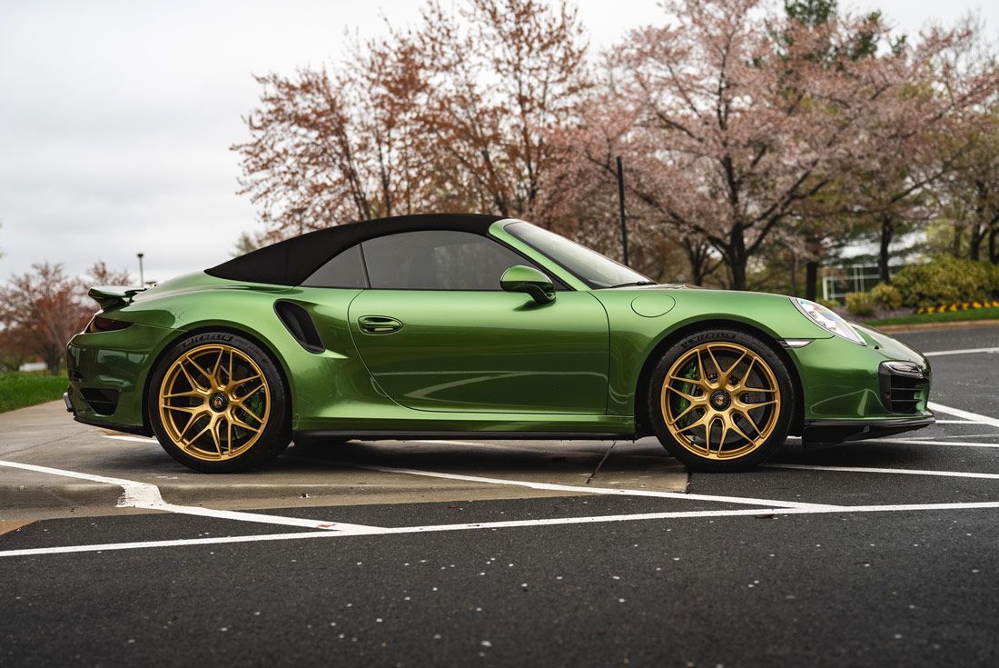 A green porsche 911 turbo s convertible is parked in a parking lot.