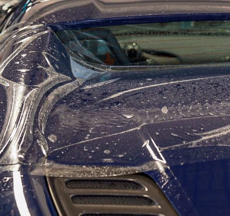 The hood of a blue sports car is covered in clear plastic