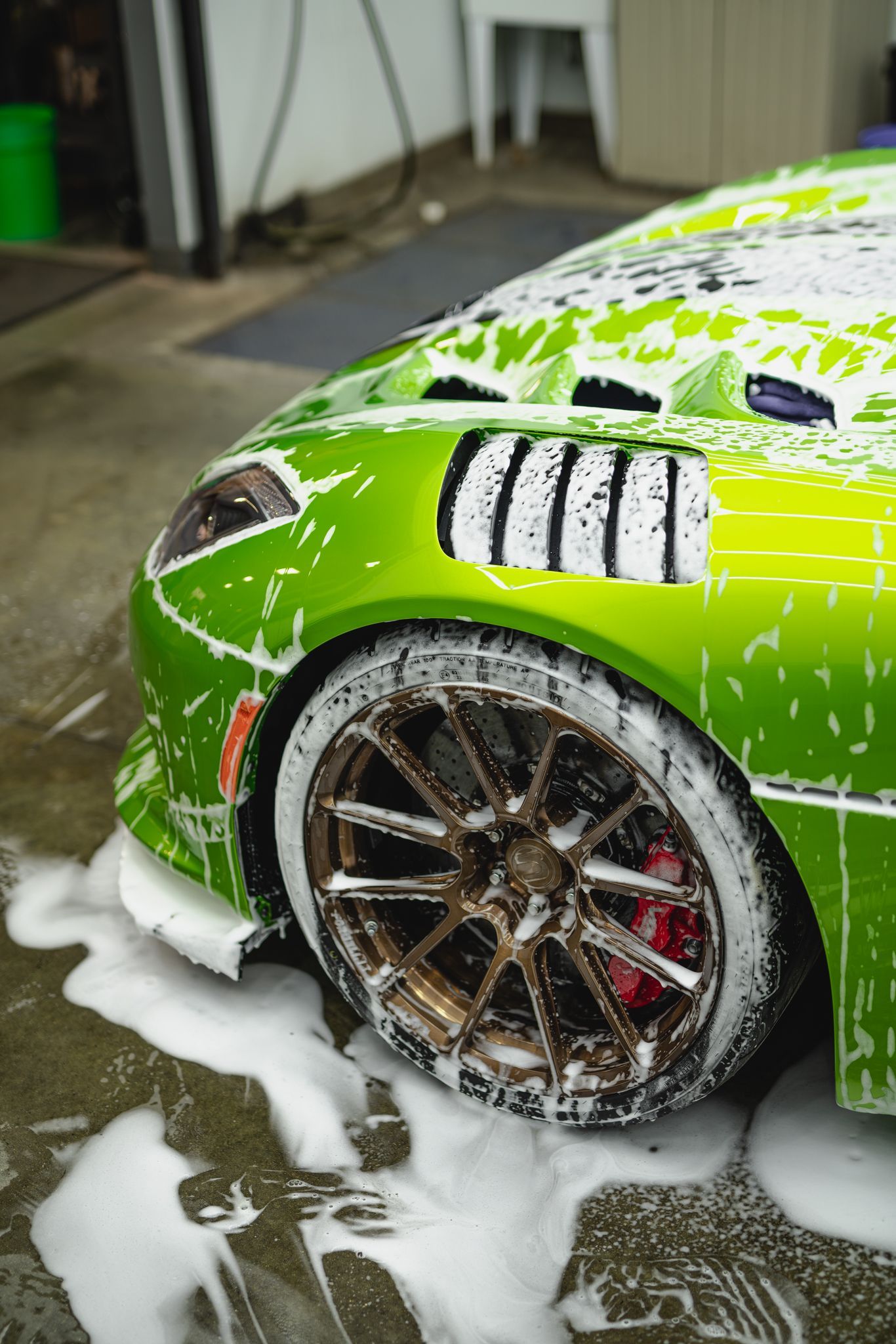 A green sports car is covered in foam at a car wash.