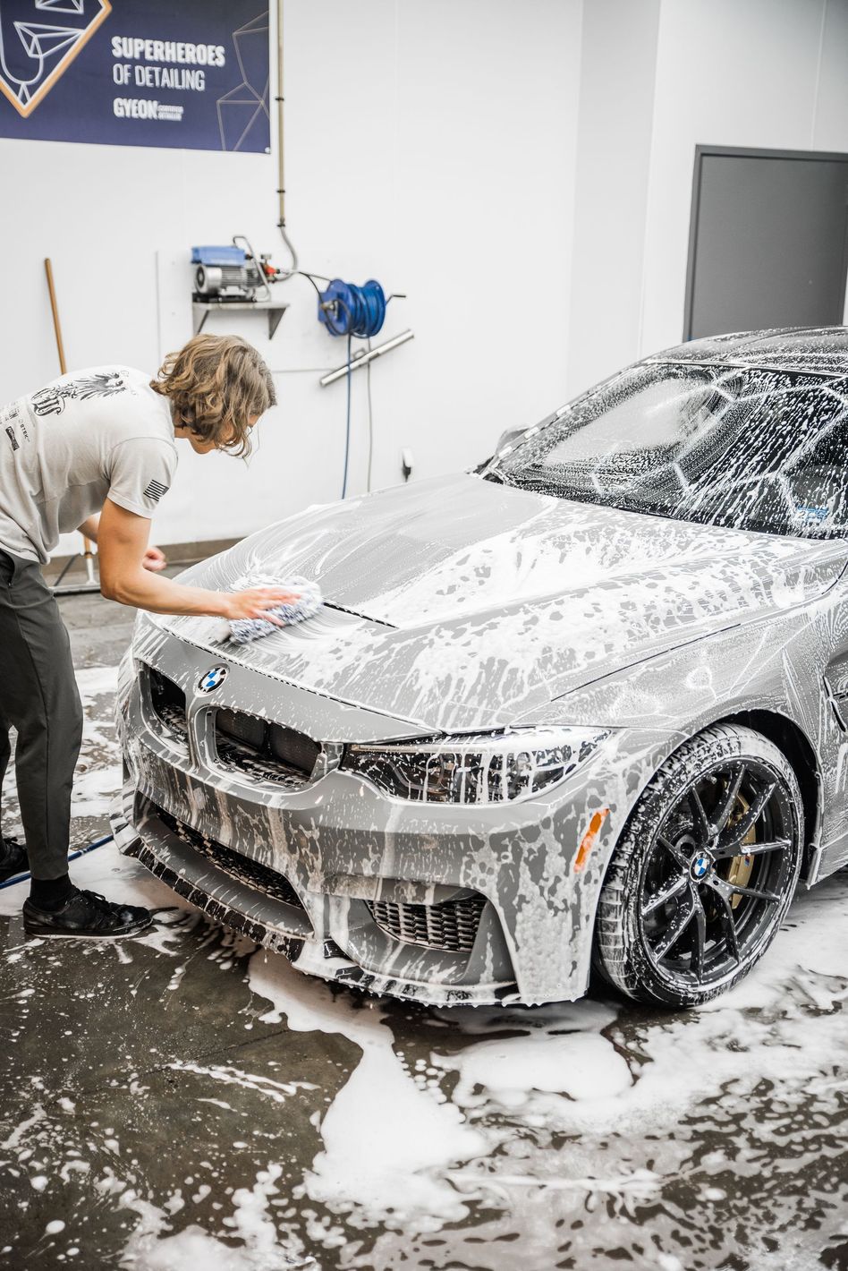 A man is washing a car with foam in a garage.