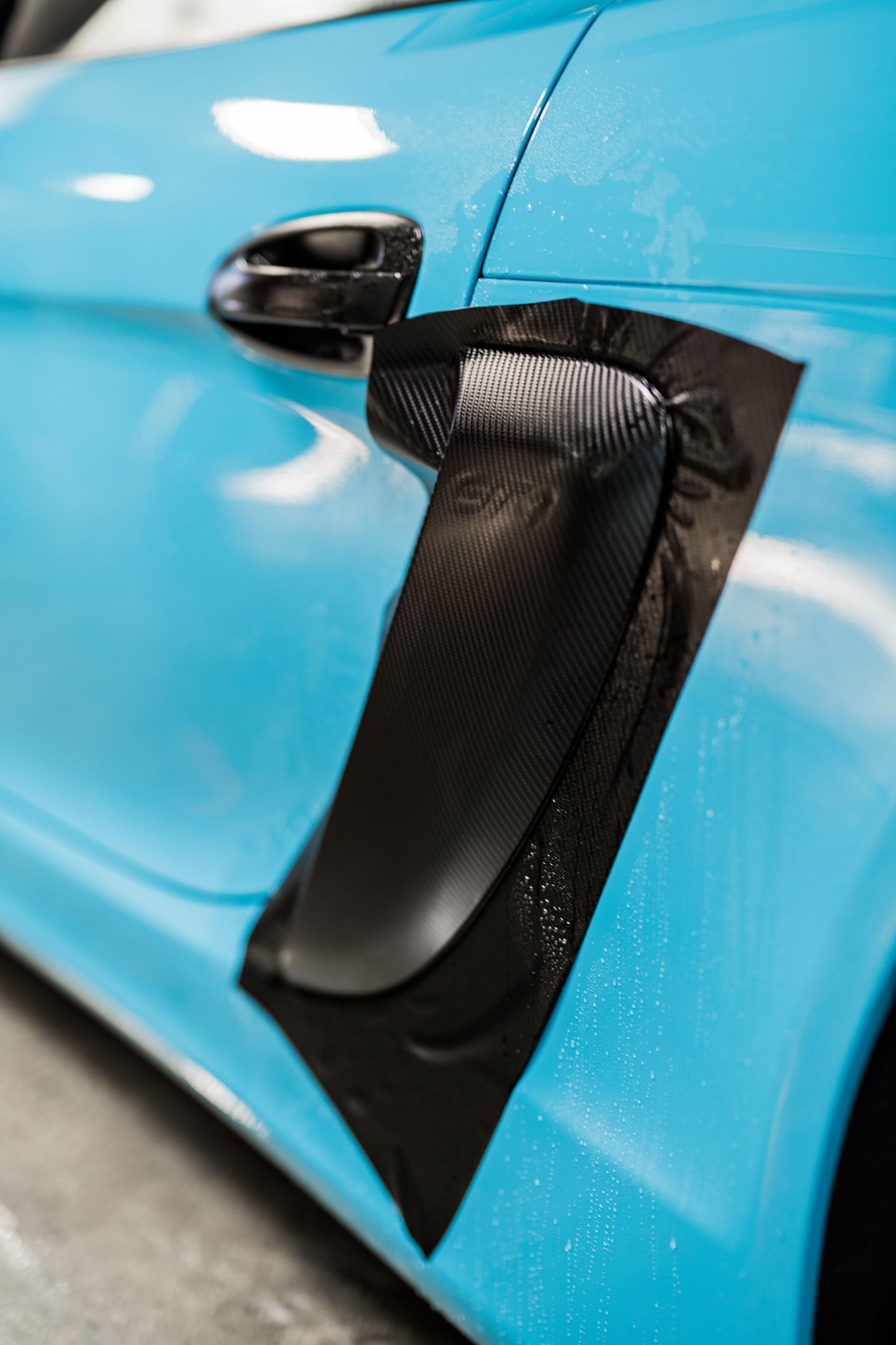 A close up of a blue car being wrapped in black tape.