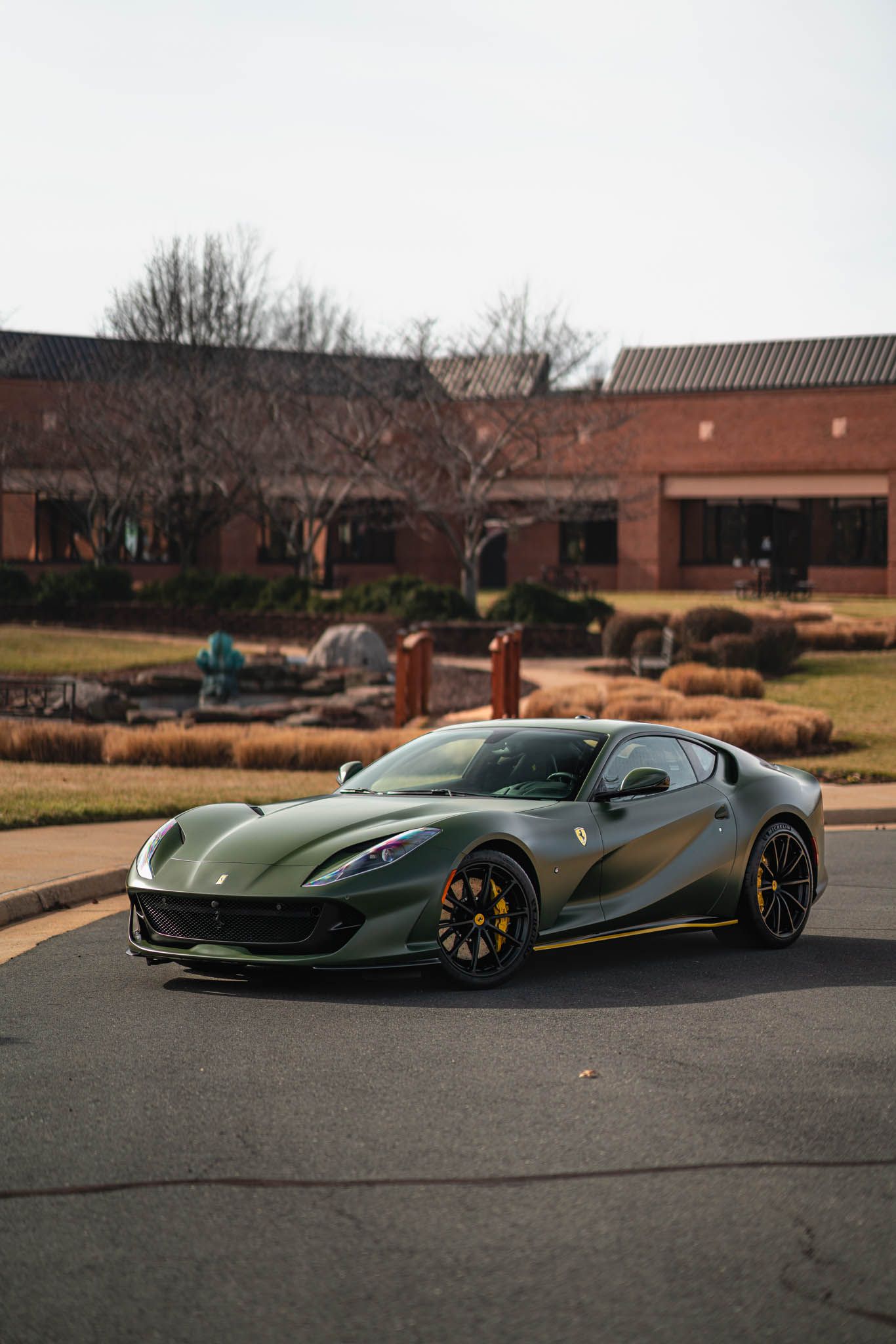 A green ferrari is parked on the side of the road in front of a brick building.