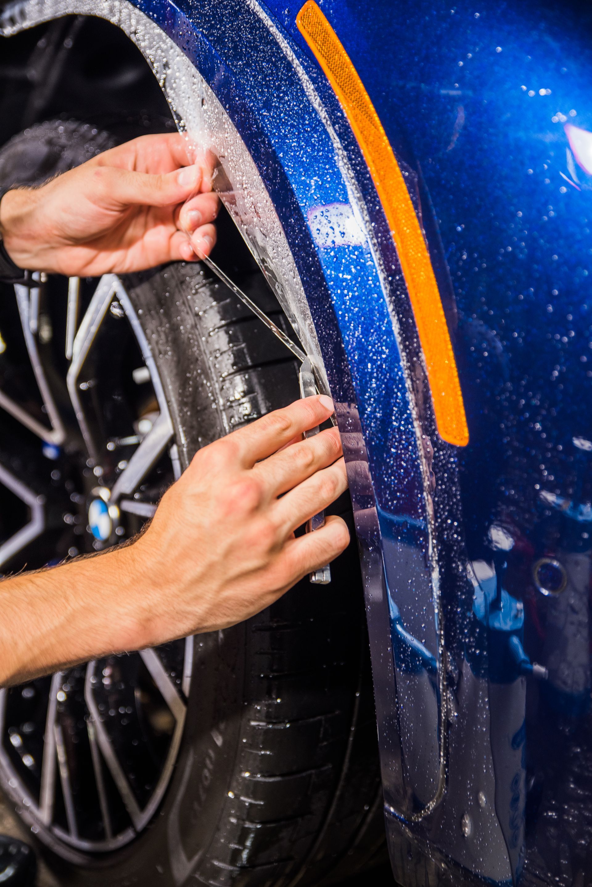 A person is applying a protective film to the fender of a blue car.