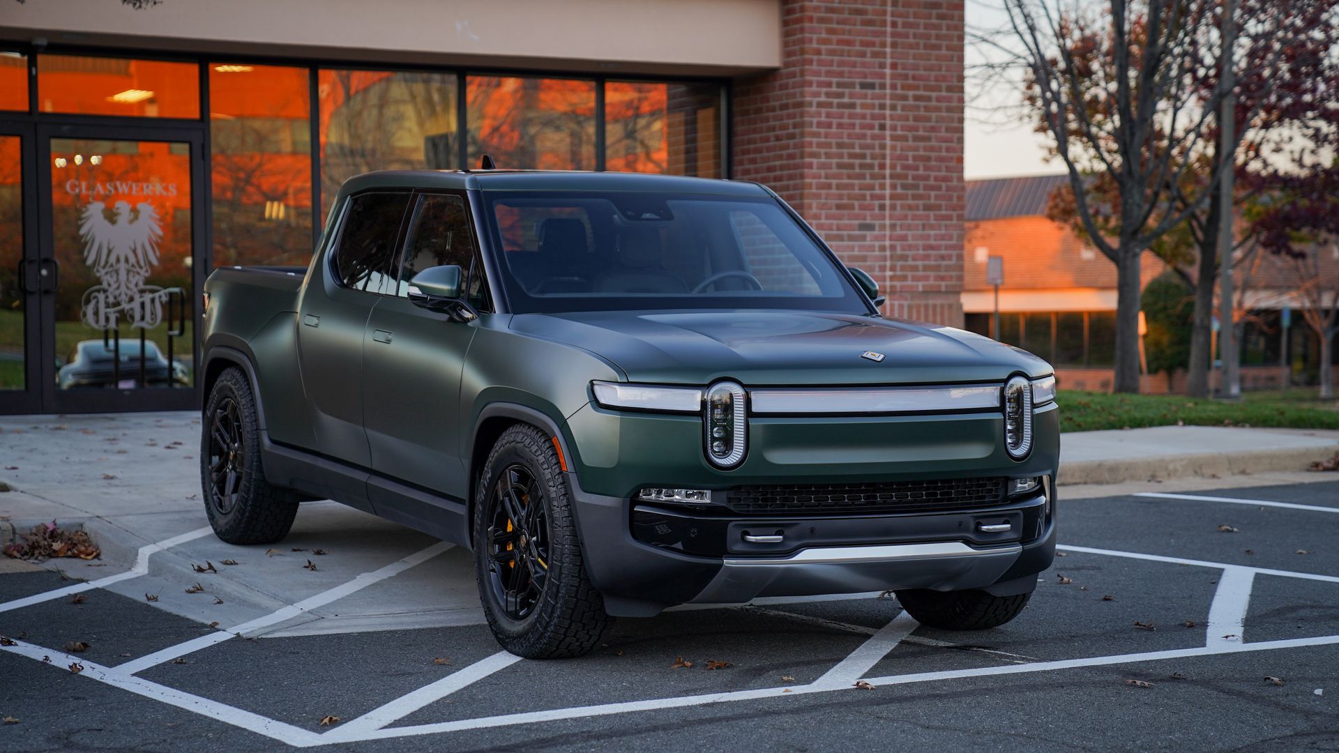 A green electric truck is parked in a parking lot in front of a building.