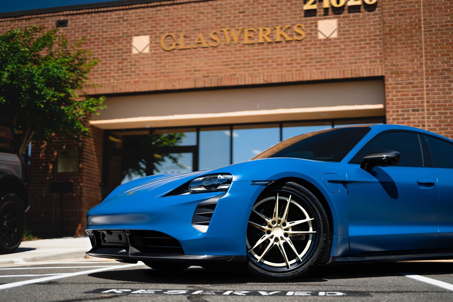 A blue porsche taycan is parked in front of a brick building.