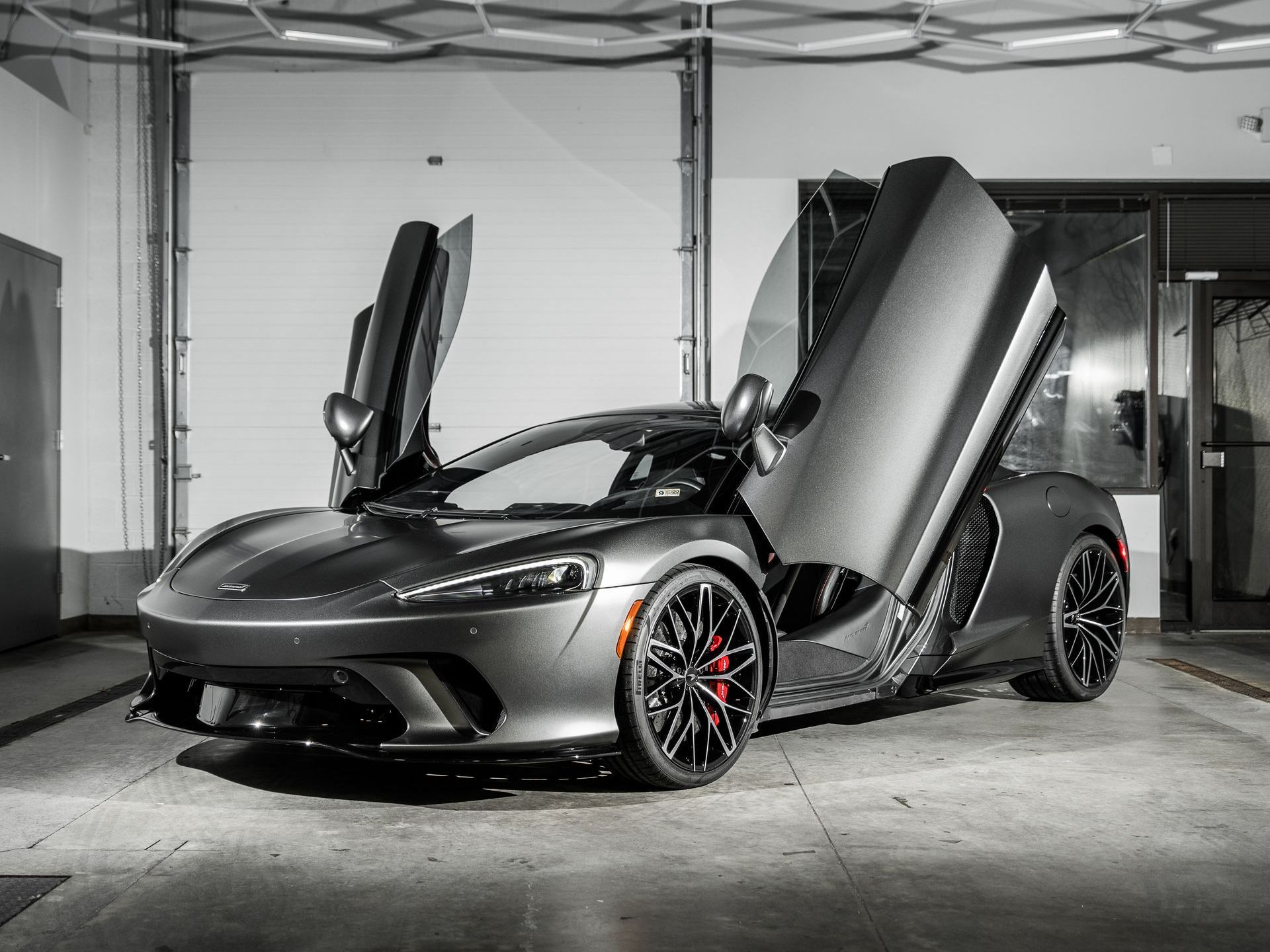 A gray sports car with its doors open is parked in a garage.