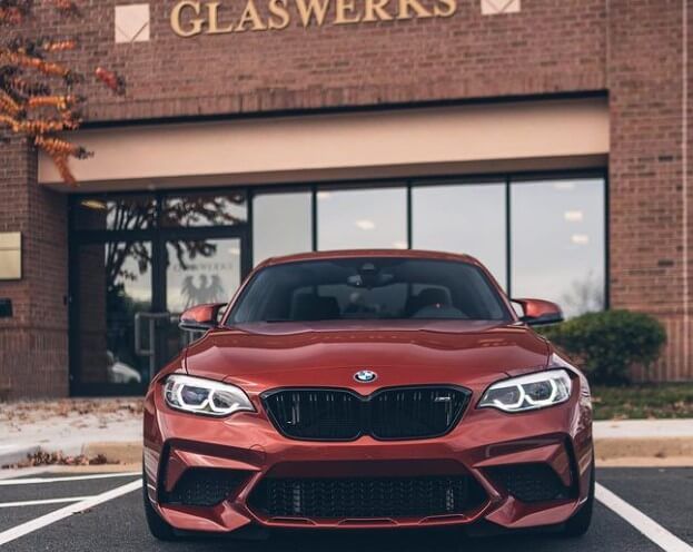 A red bmw is parked in front of a glassworks building