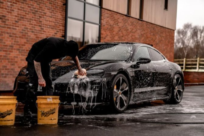 A man is washing a black car in a parking lot.