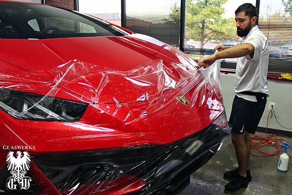 A man is wrapping a red car with plastic wrap.