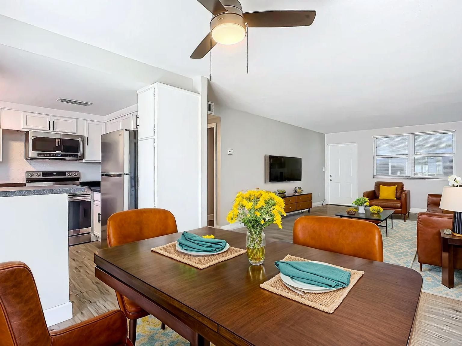 Open-concept living space with dining table, kitchen, and living room; brown and orange tones.
