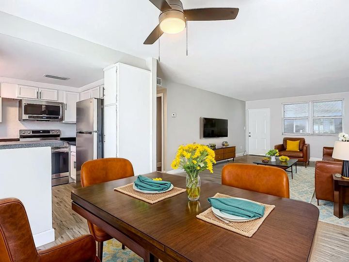 Open-concept living space with dining table, kitchen, and living room; brown and orange tones.