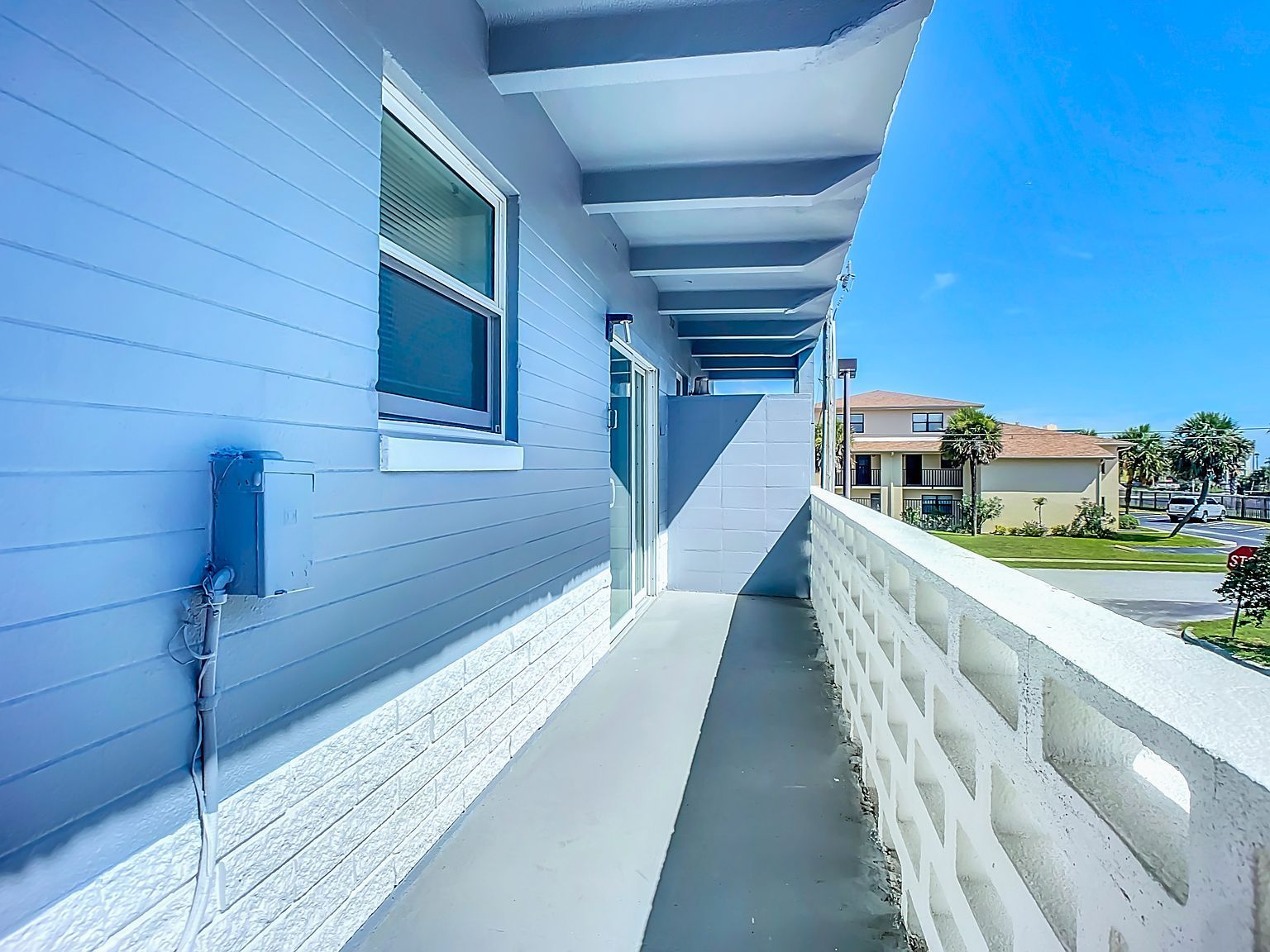 Exterior balcony with a gray floor, blue wall, and white block railing on a sunny day.