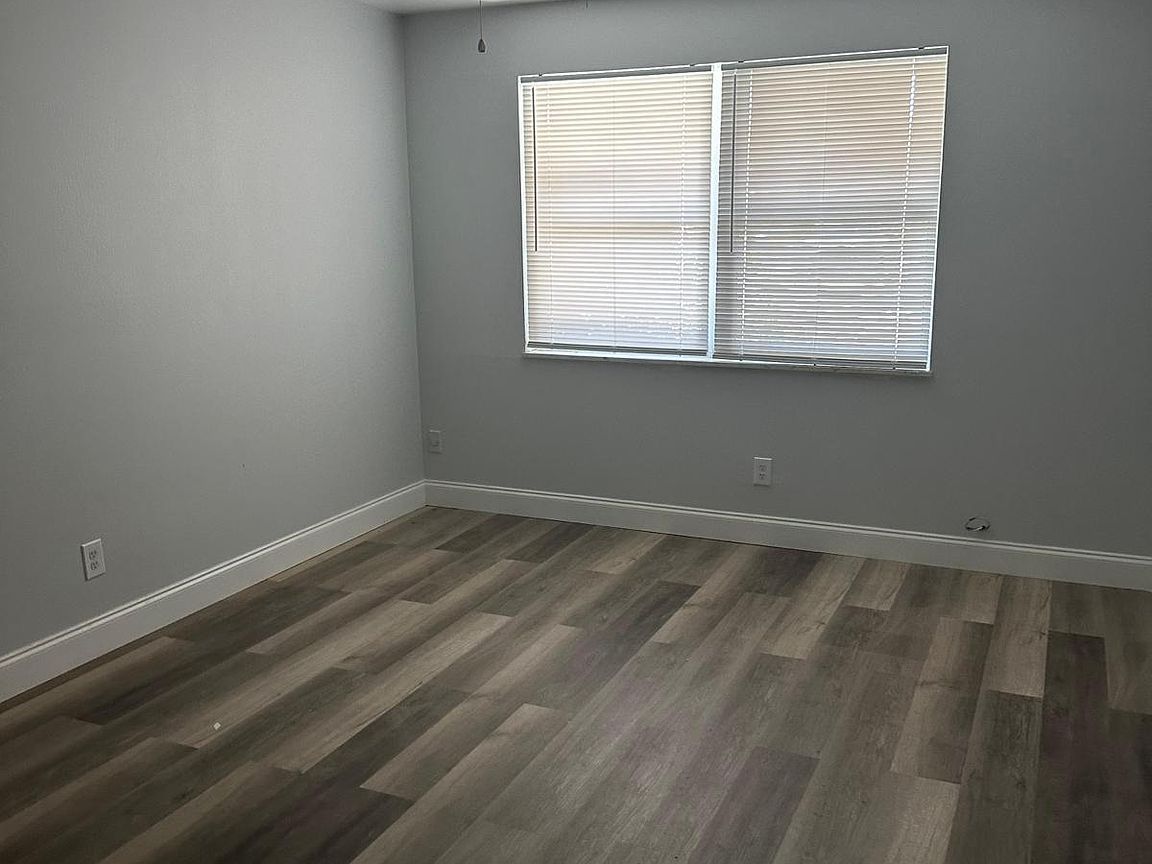 Empty room with gray walls, wood-look flooring, and a window with closed blinds.