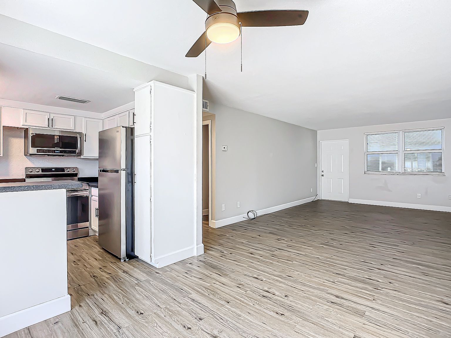 Open-concept kitchen and living area with white cabinets, stainless steel appliances, and wood-look flooring.