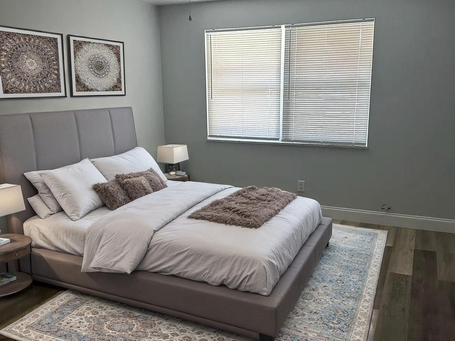 Bedroom with bed, art, rug, and window with blinds; gray and neutral tones.