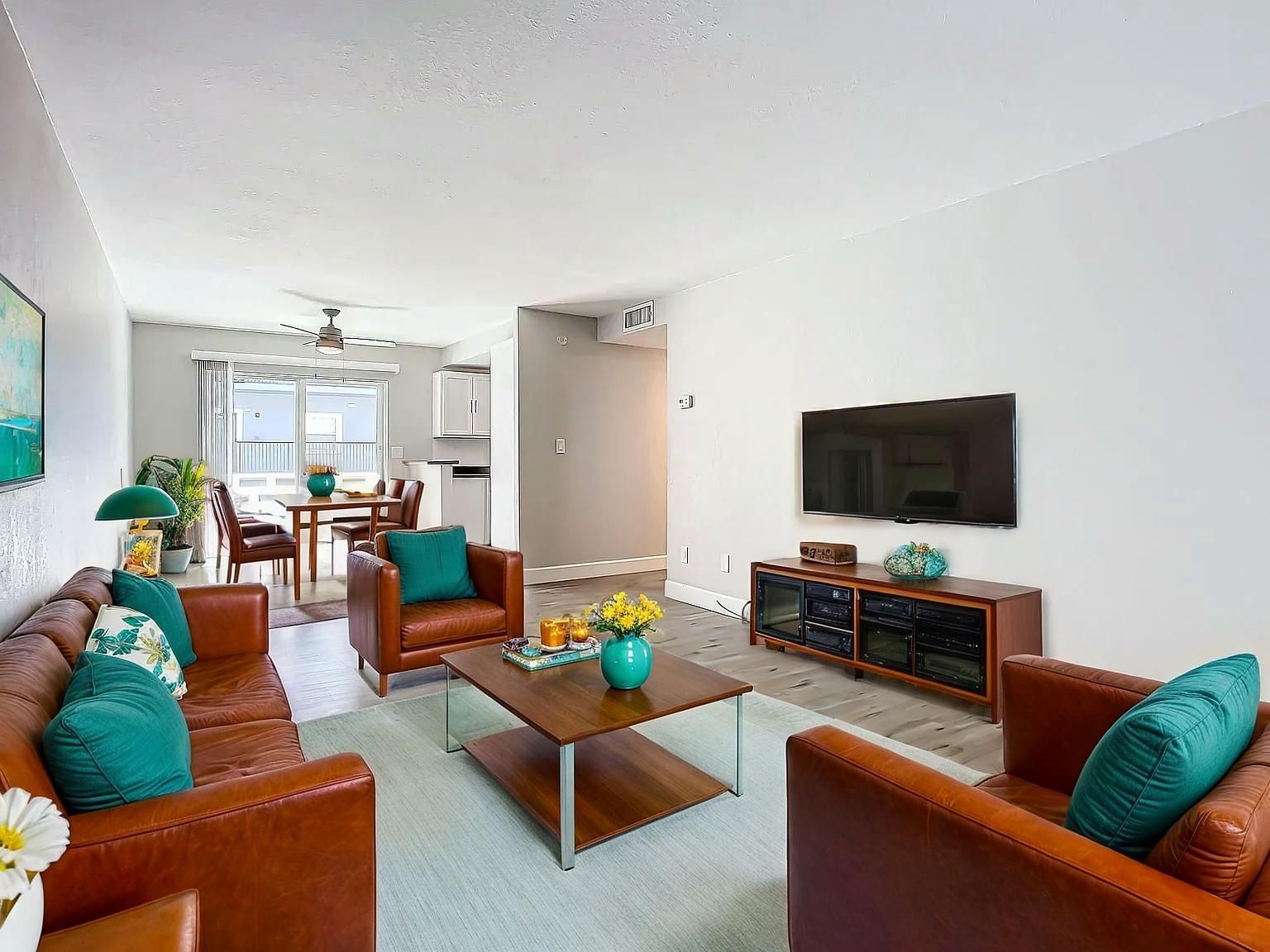 Living room with brown leather sofa and chairs, teal accents, TV, and dining area.