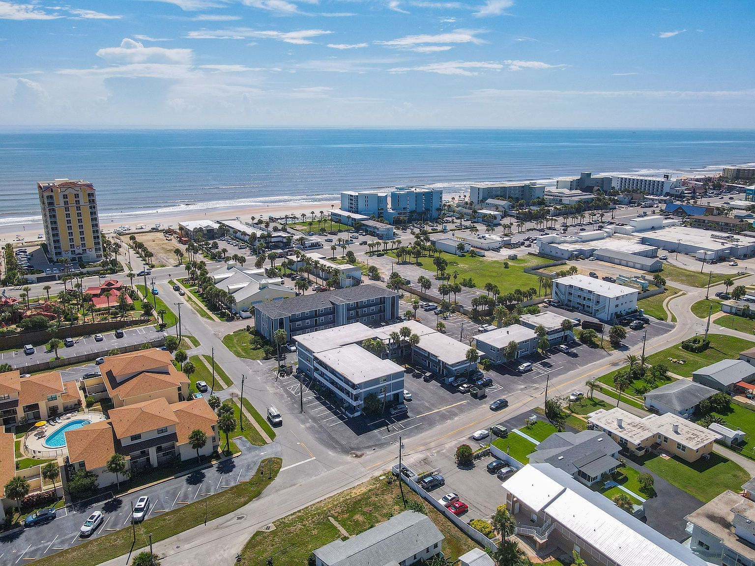 Aerial view of a coastal town with buildings, beach, and ocean under a blue sky.
