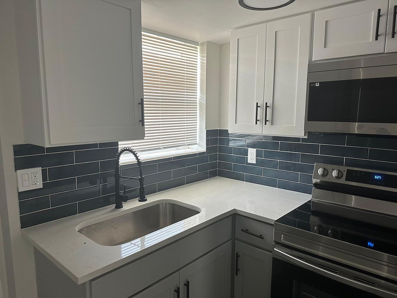 Modern kitchen with white cabinets, stainless steel appliances, and gray backsplash.