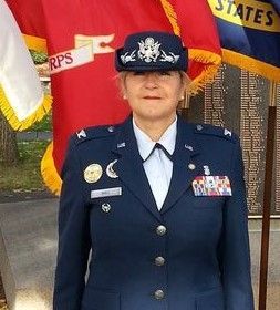 Female in Air Force uniform stands outdoors with flags.