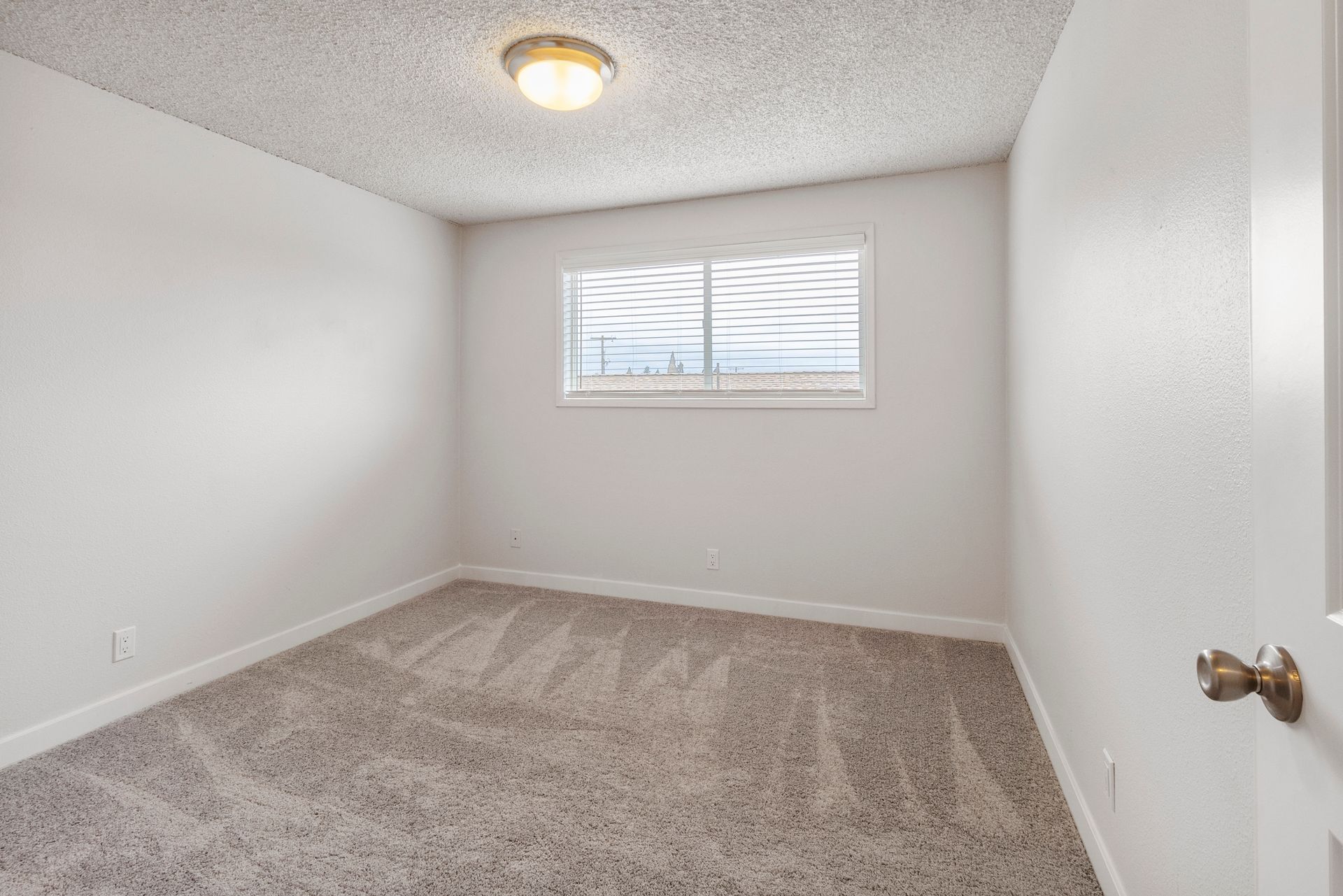 An empty bedroom with a window and a carpeted floor.