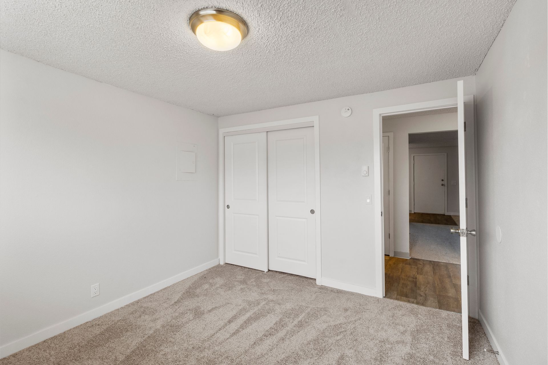 An empty bedroom with a closet and a door leading to a hallway.