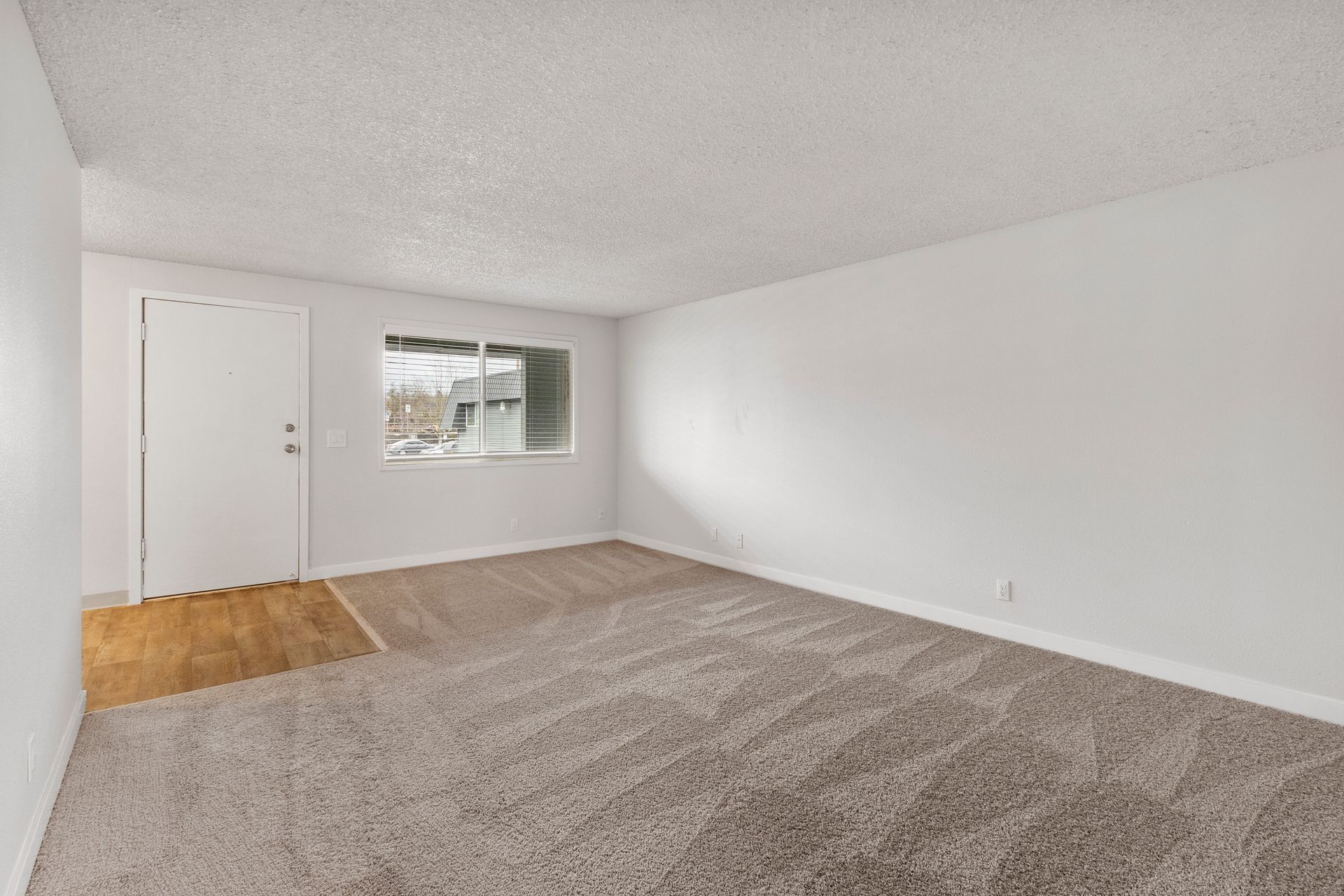 An empty living room with a carpeted floor , white walls and a window.
