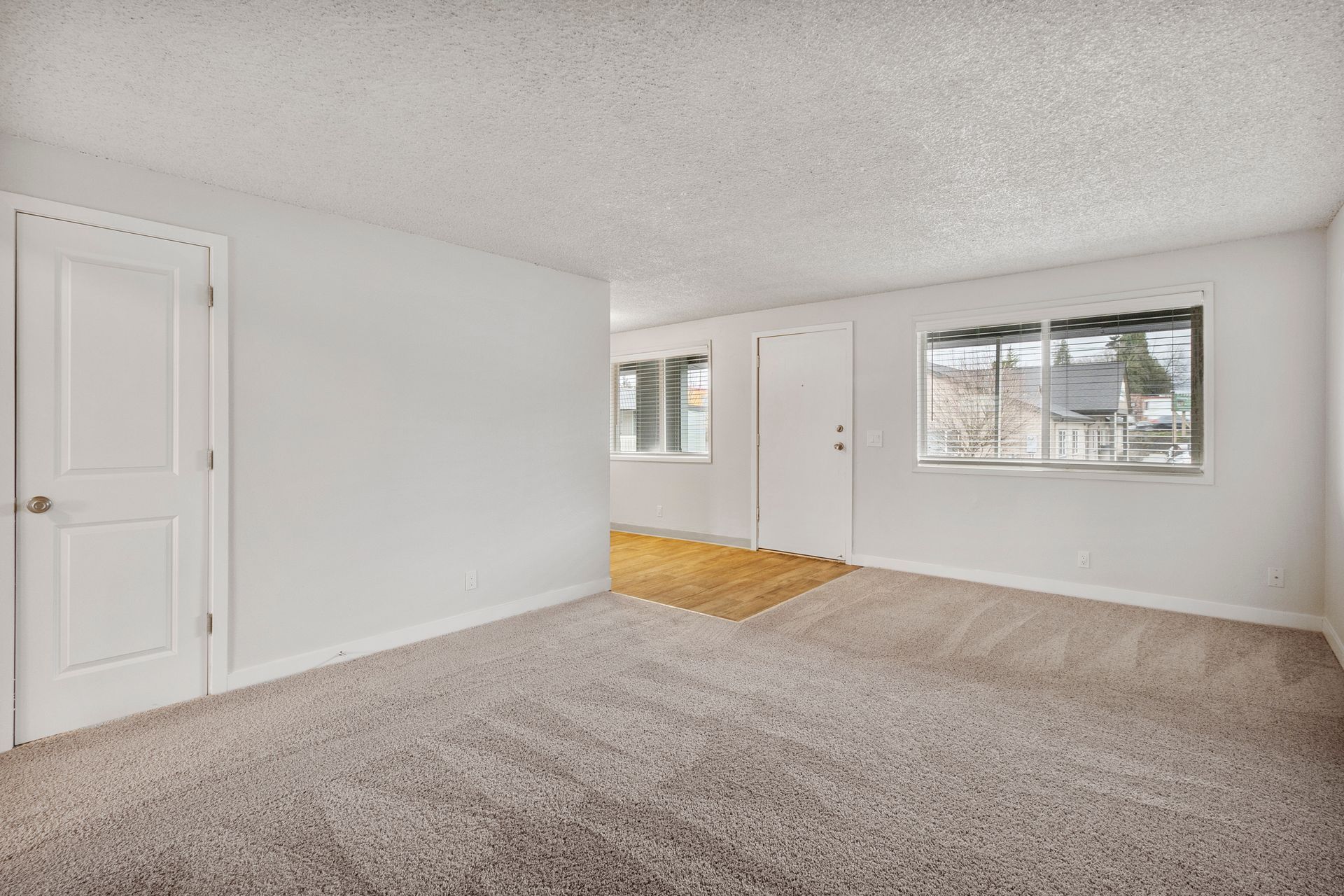 An empty living room with a carpeted floor and white walls.