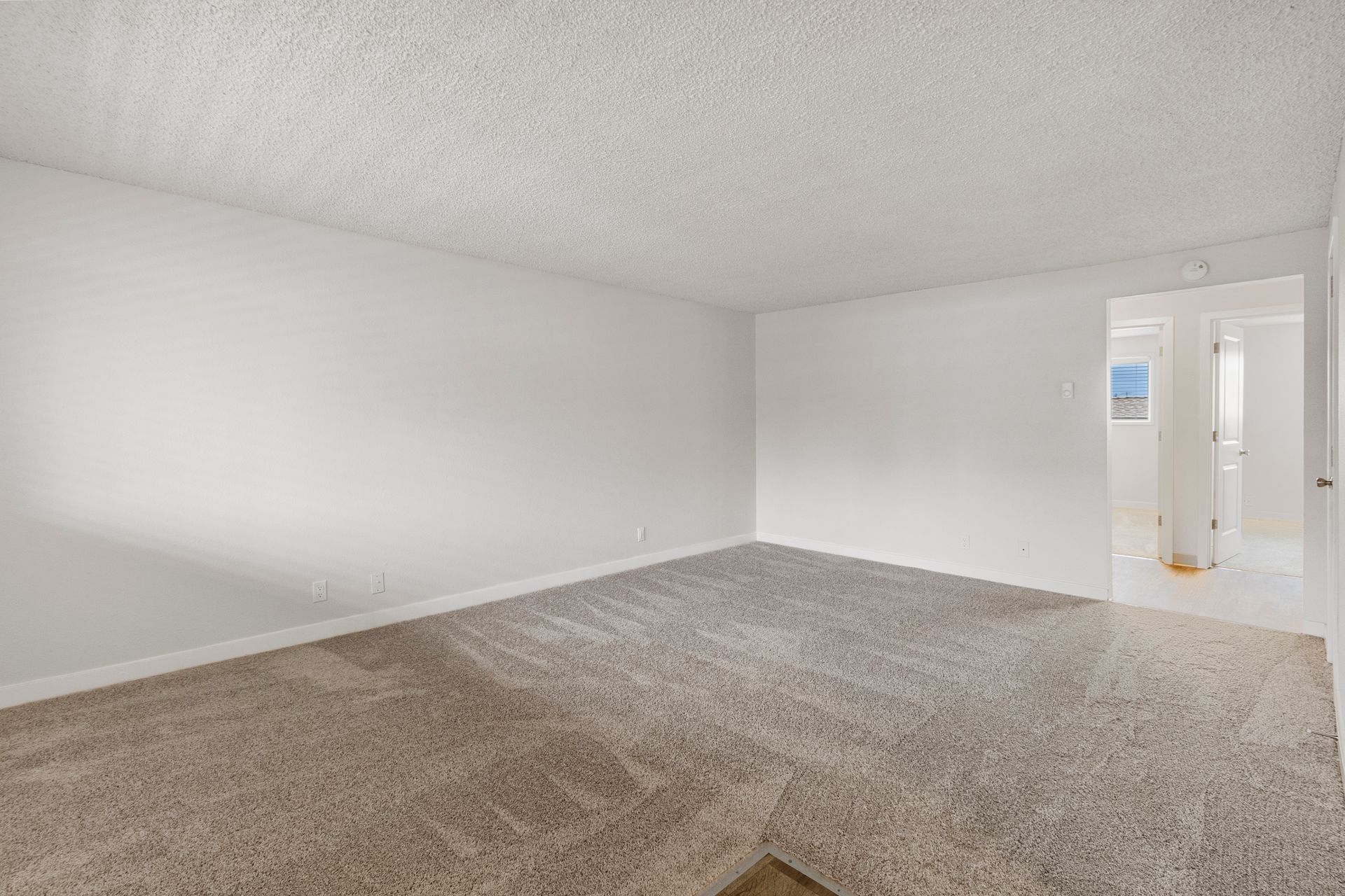 An empty living room with a carpeted floor and white walls.