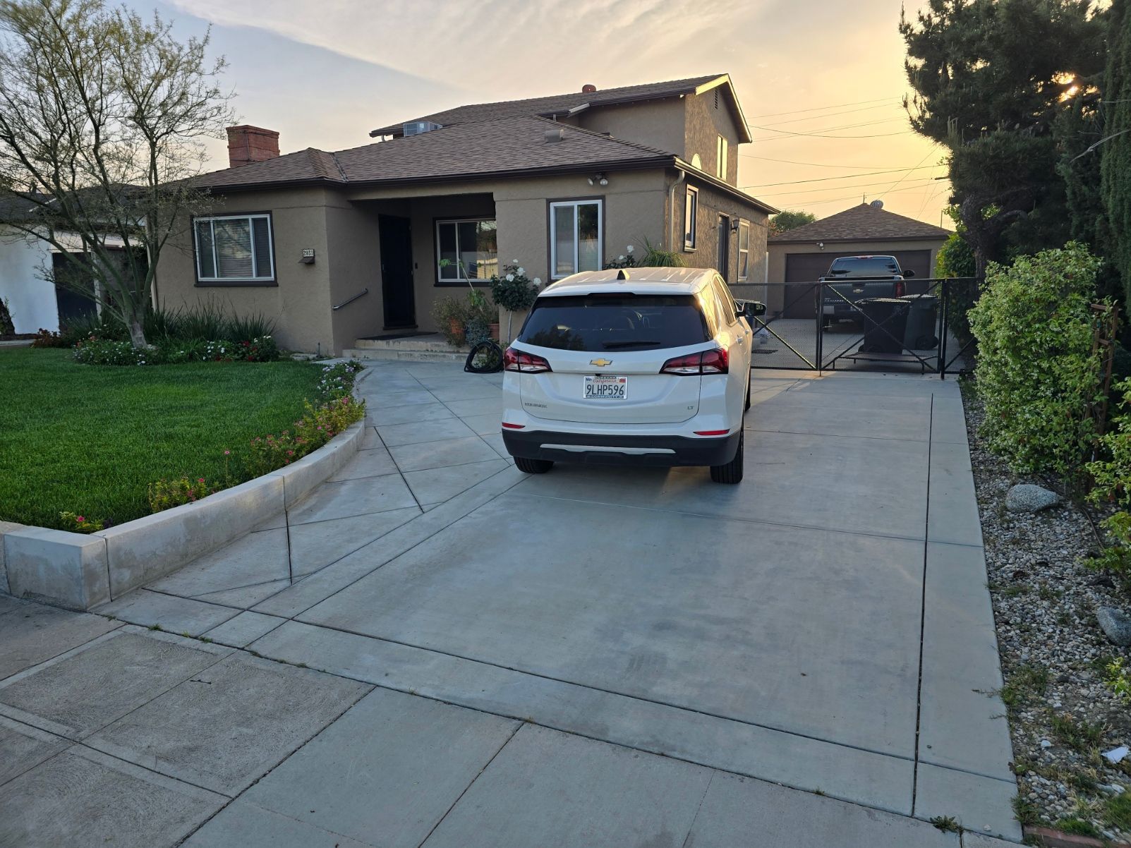 A car parked in a driveway with concrete slabs in front of a house on a sunny day.