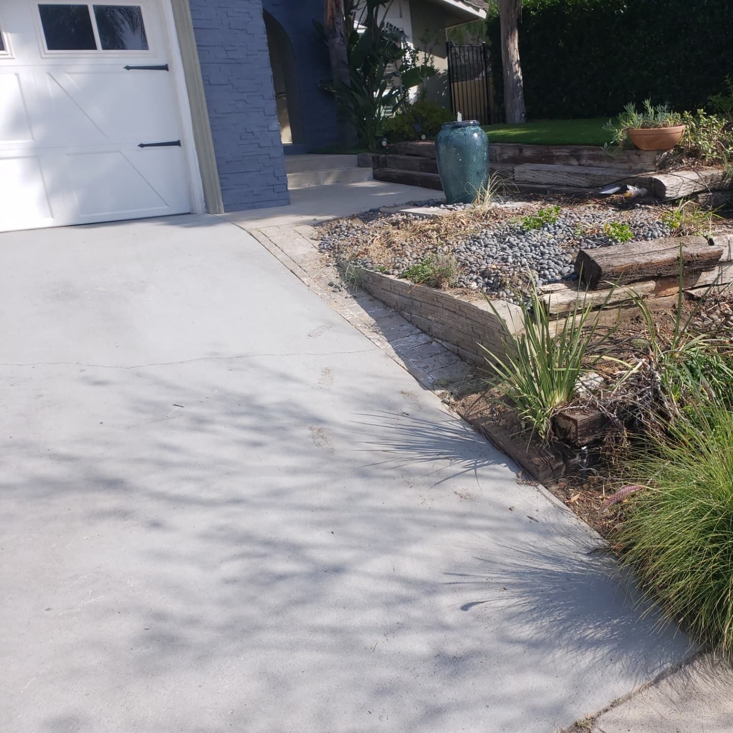 Driveway next to a garden bed with log border, leading to a garage. Sunny day.