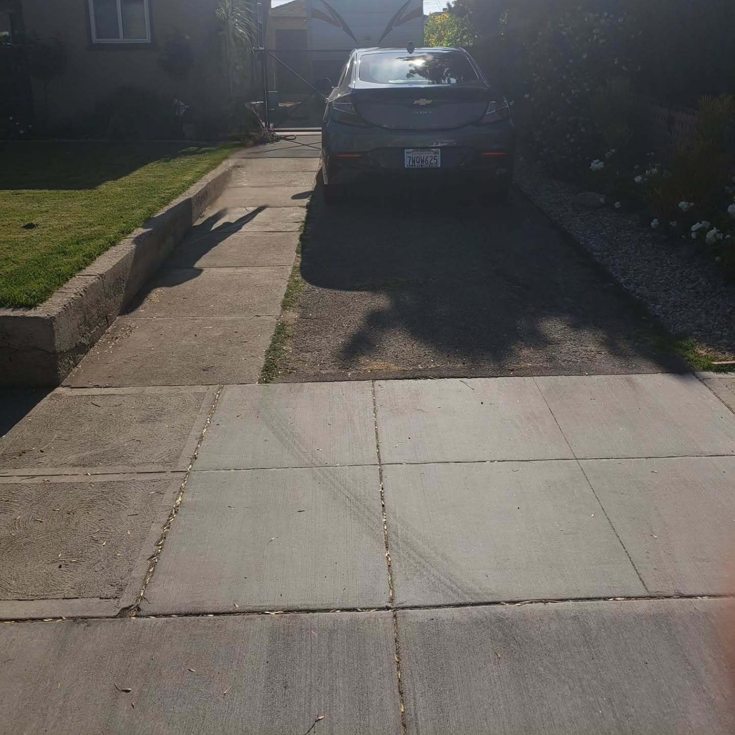 Driveway with car parked, sidewalk on left, grassy area, sunny day.