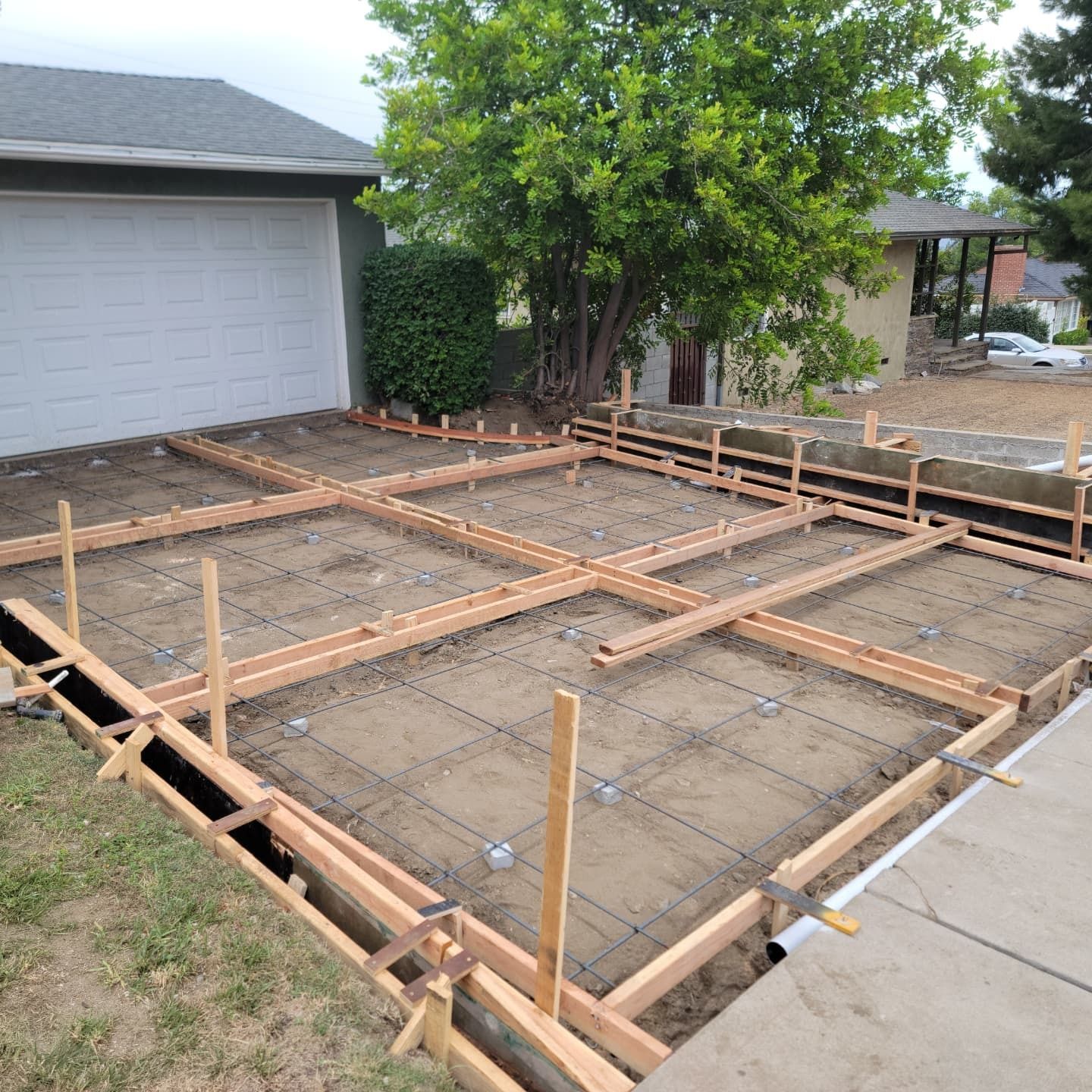 Wooden forms and rebar frame a driveway area, ready for concrete, next to a garage.
