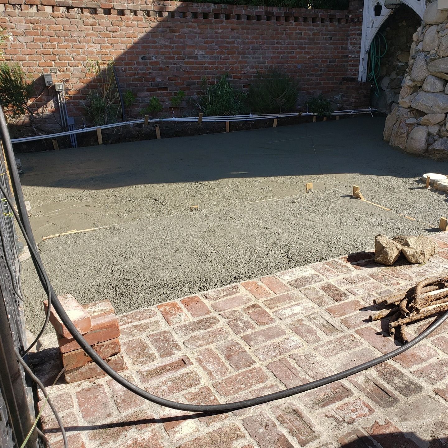 Freshly poured concrete in a backyard, next to a brick patio and wall.